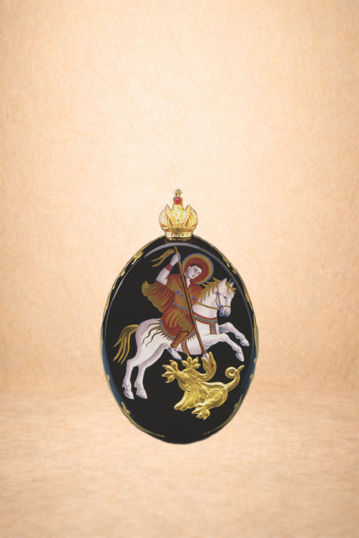 A black oval object featuring a religious image of a saint riding a white horse, holding a spear, with a gold dragon at the bottom, topped with a gold crown, on a plain beige background.