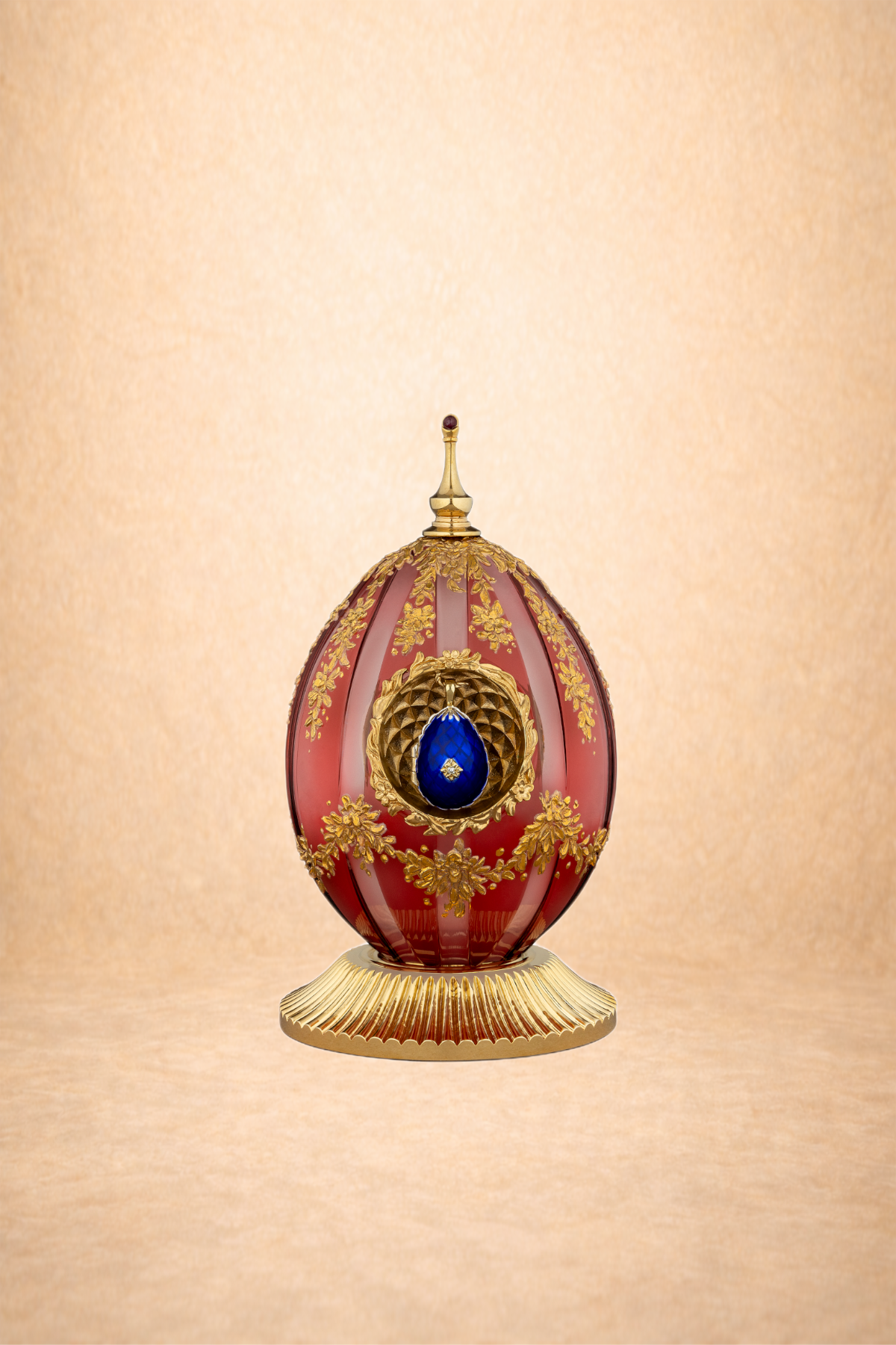 An ornate decorative egg with gold accents, a blue gemstone, and floral motifs, displayed on a gold stand against a beige background.