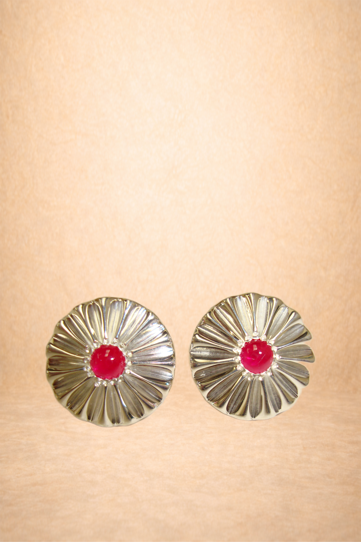 Pair of silver flower-shaped earrings with pink centers on a beige background.