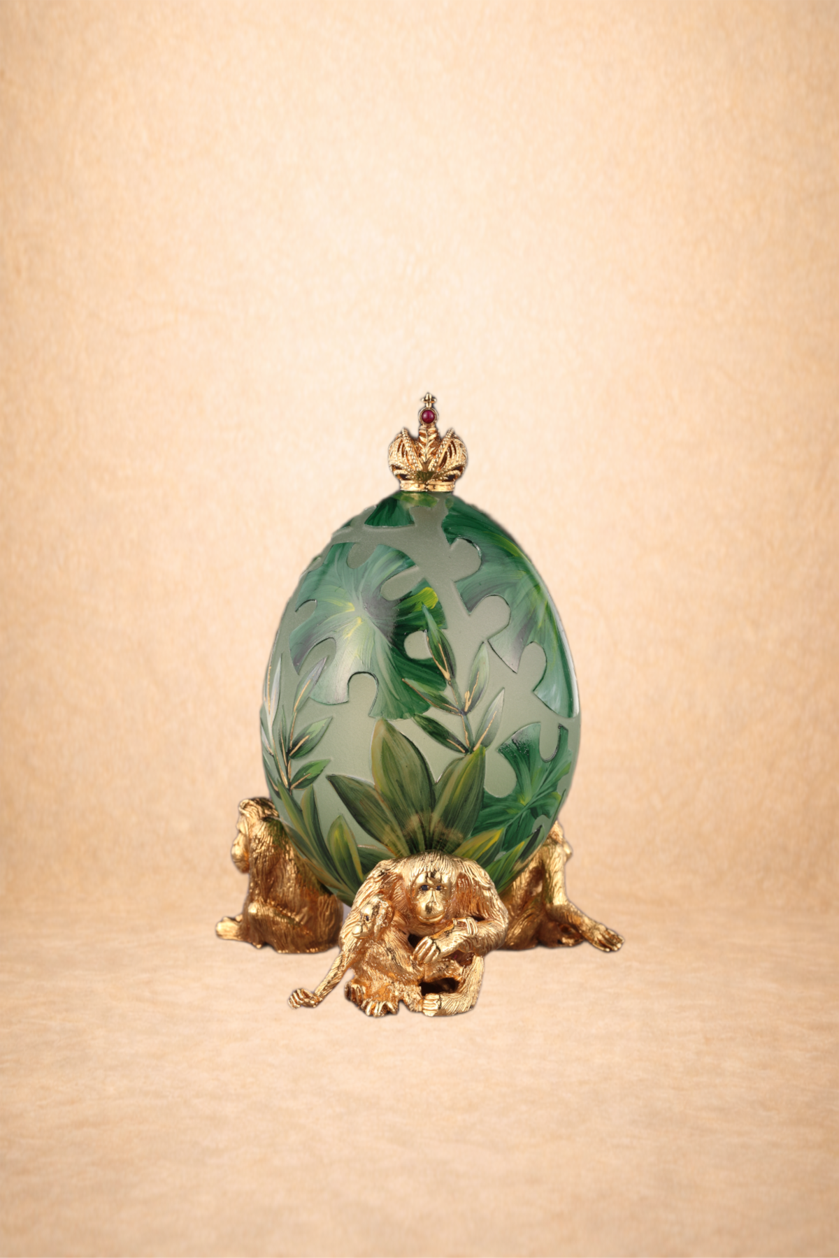 An ornate decorative egg with green leafy patterns, topped with a small golden crown, and supported by detailed golden monkey figures at the base.