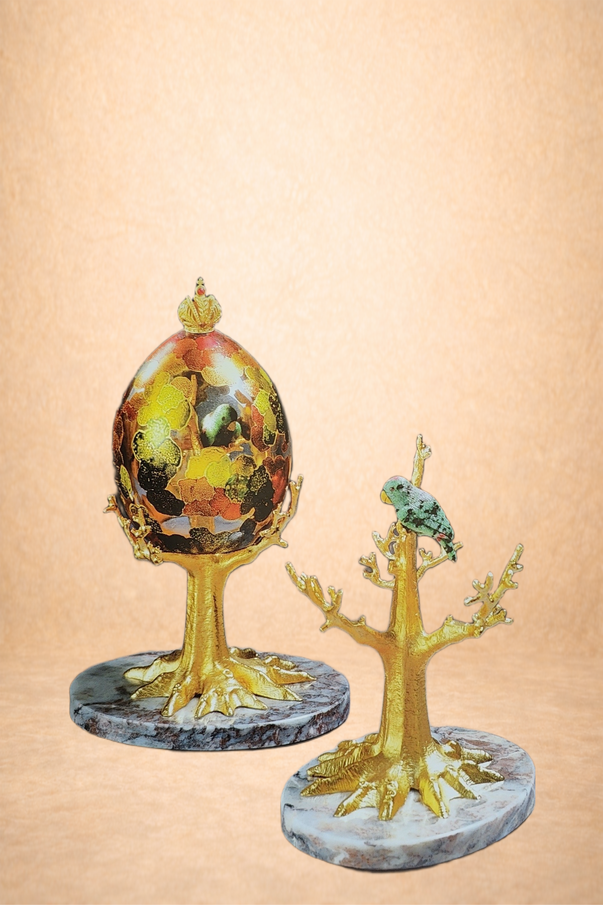 Decorative ornaments featuring gold-colored tree bases with marble bases. One ornament has a multicolored, patterned egg on top, and the other has a small bird perched on a branch.