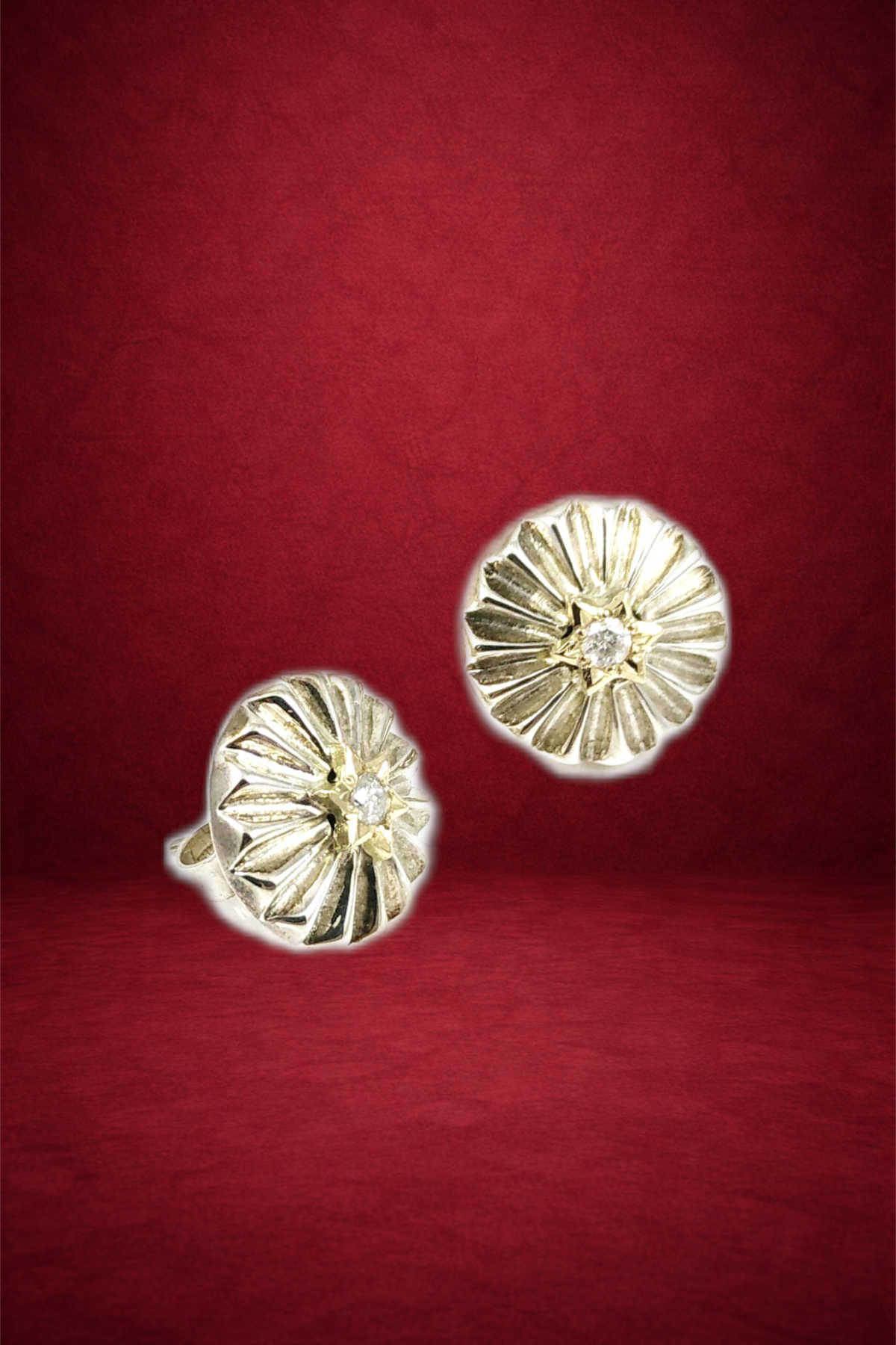 Gold and silver floral-shaped earrings with small central diamonds placed on a red background.