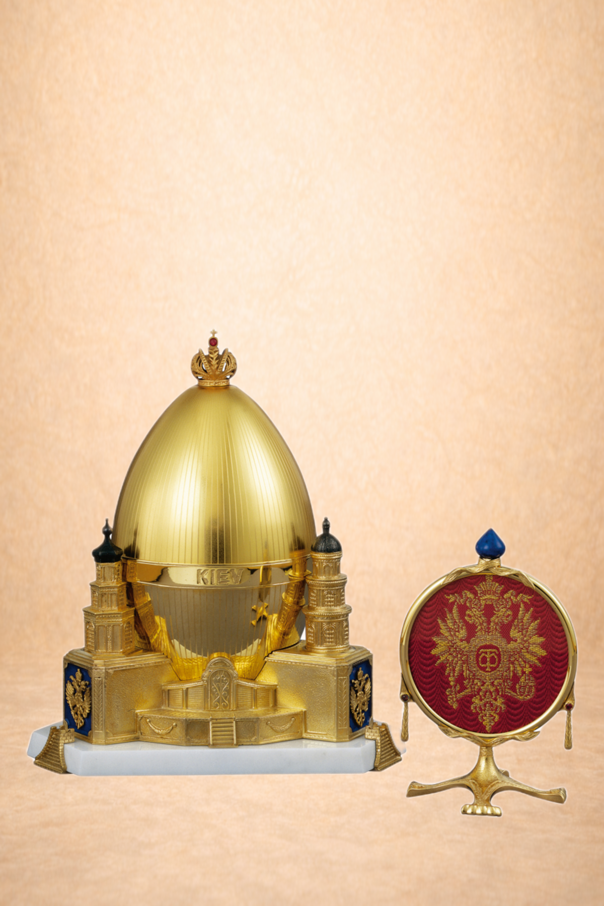 A golden model of a cathedral with a large central dome, smaller domes, and the word 'KIEV' written on it, accompanied by a small, ornate red and gold emblem featuring a double-headed eagle and a crown.