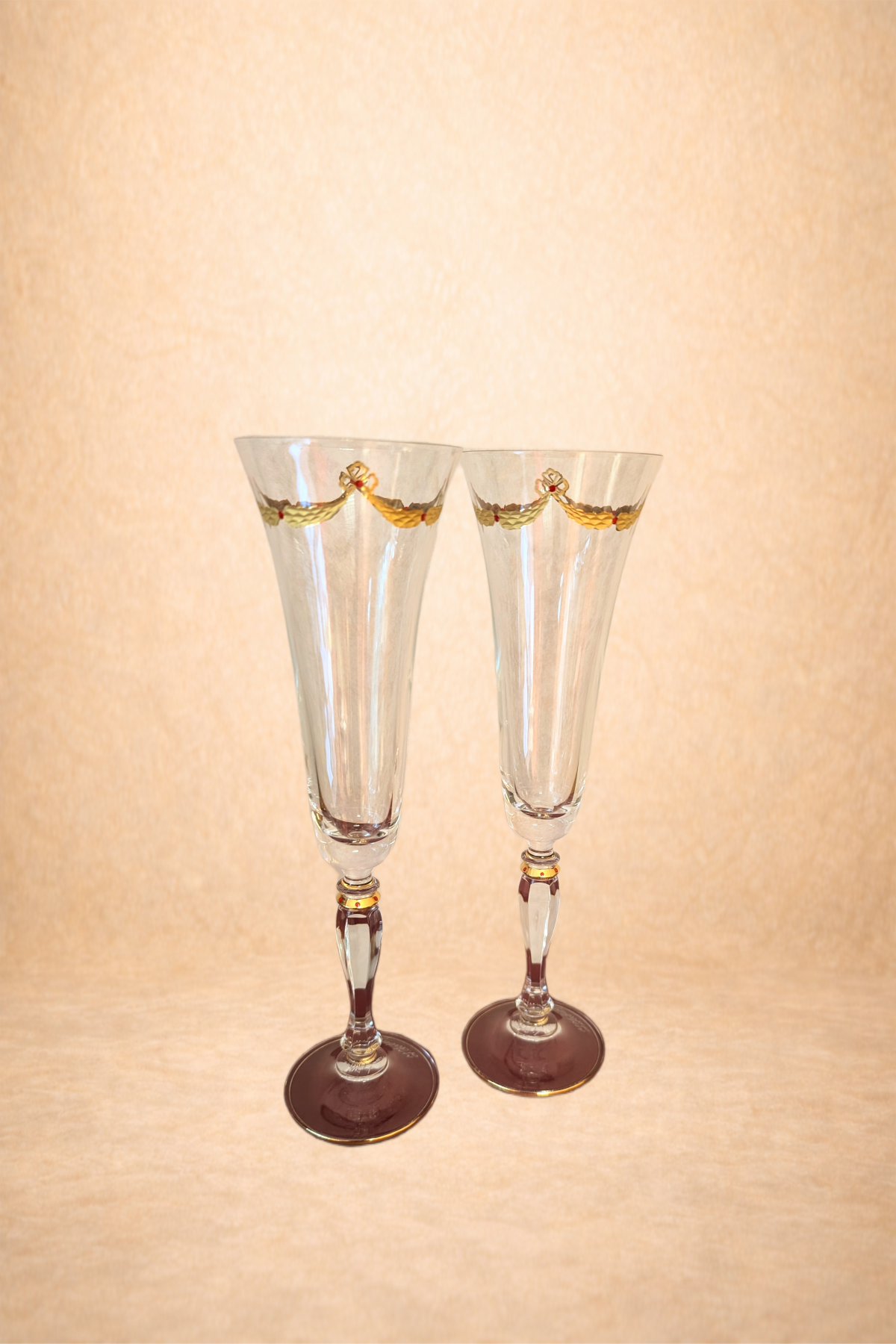 Two tall, clear champagne flutes with gold accents and decorative swags near the rim, set against a neutral background.