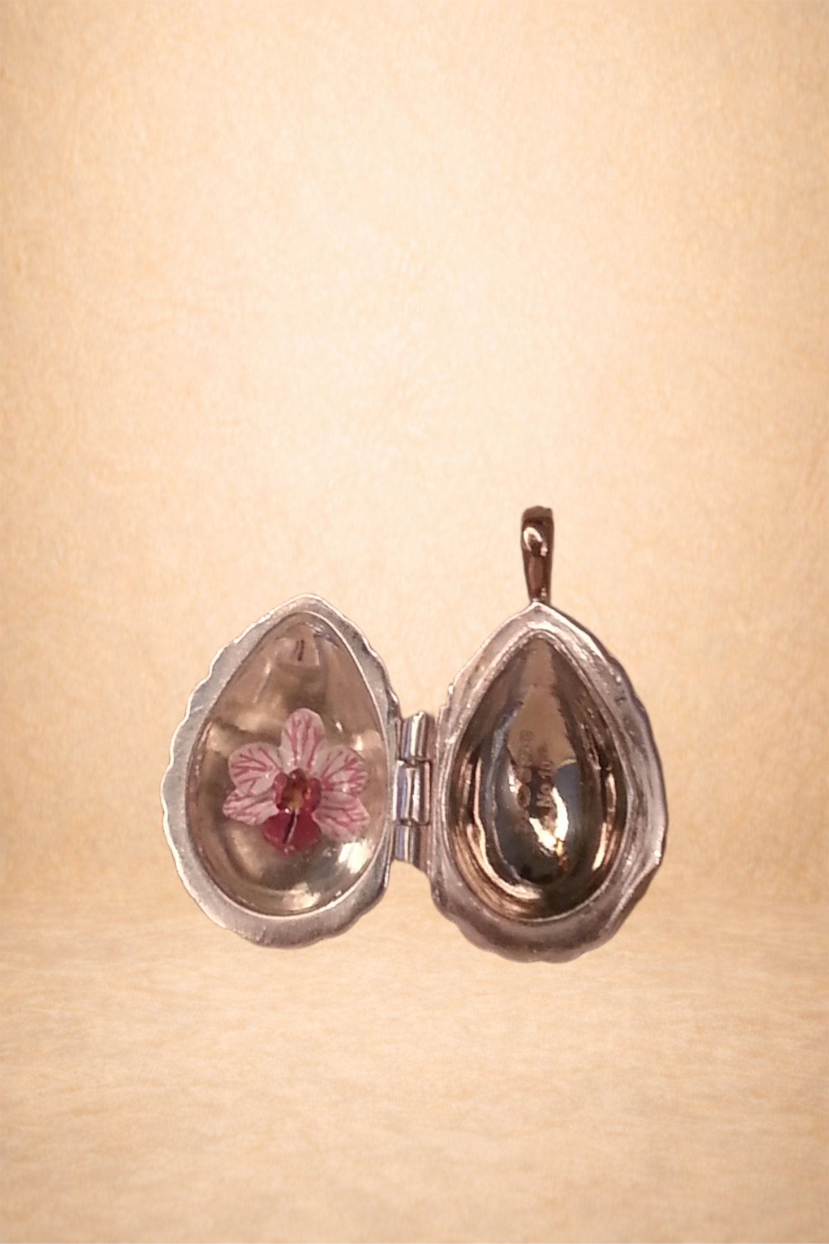A small, silver, heart-shaped jewelry box with an orchid inside, open and resting on a beige surface.