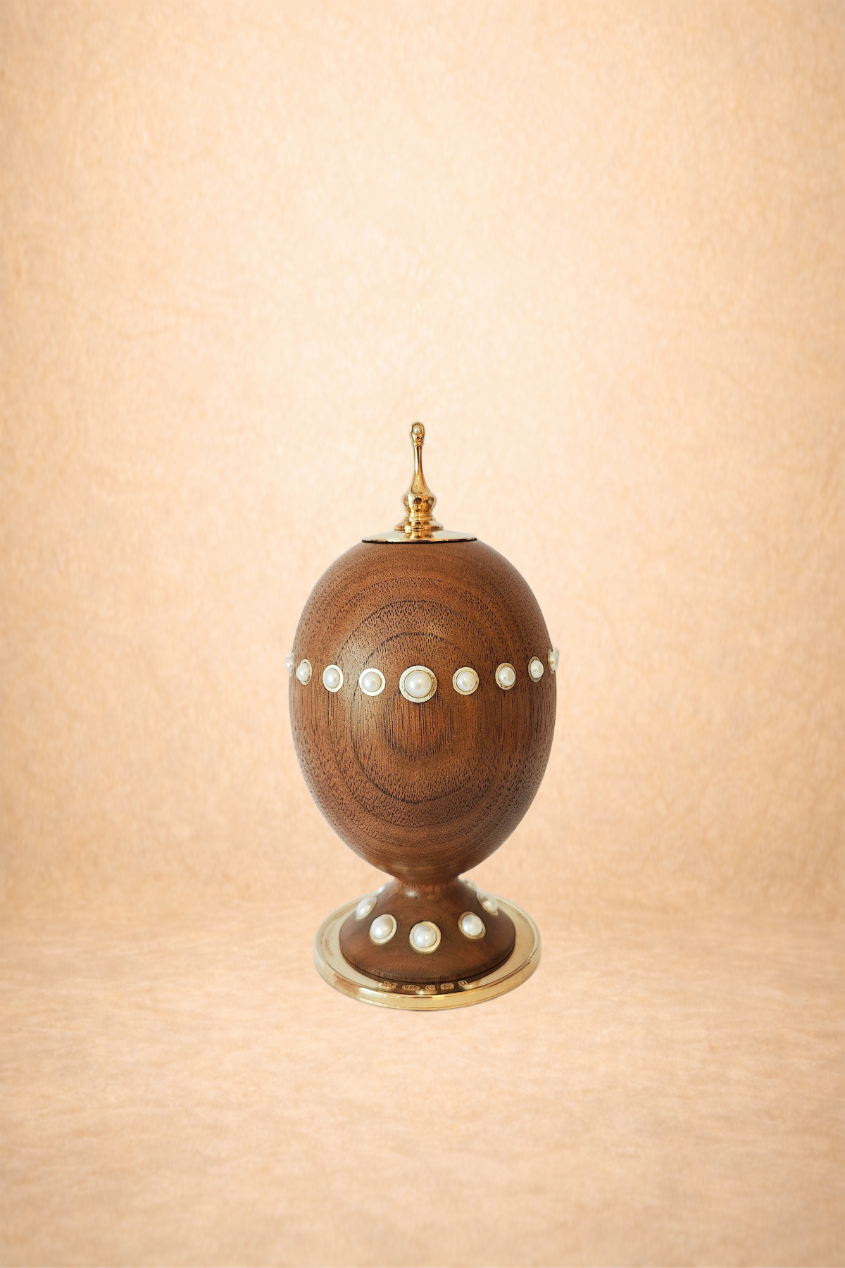 A decorative wooden egg-shaped box with pearl accents on a transparent stand