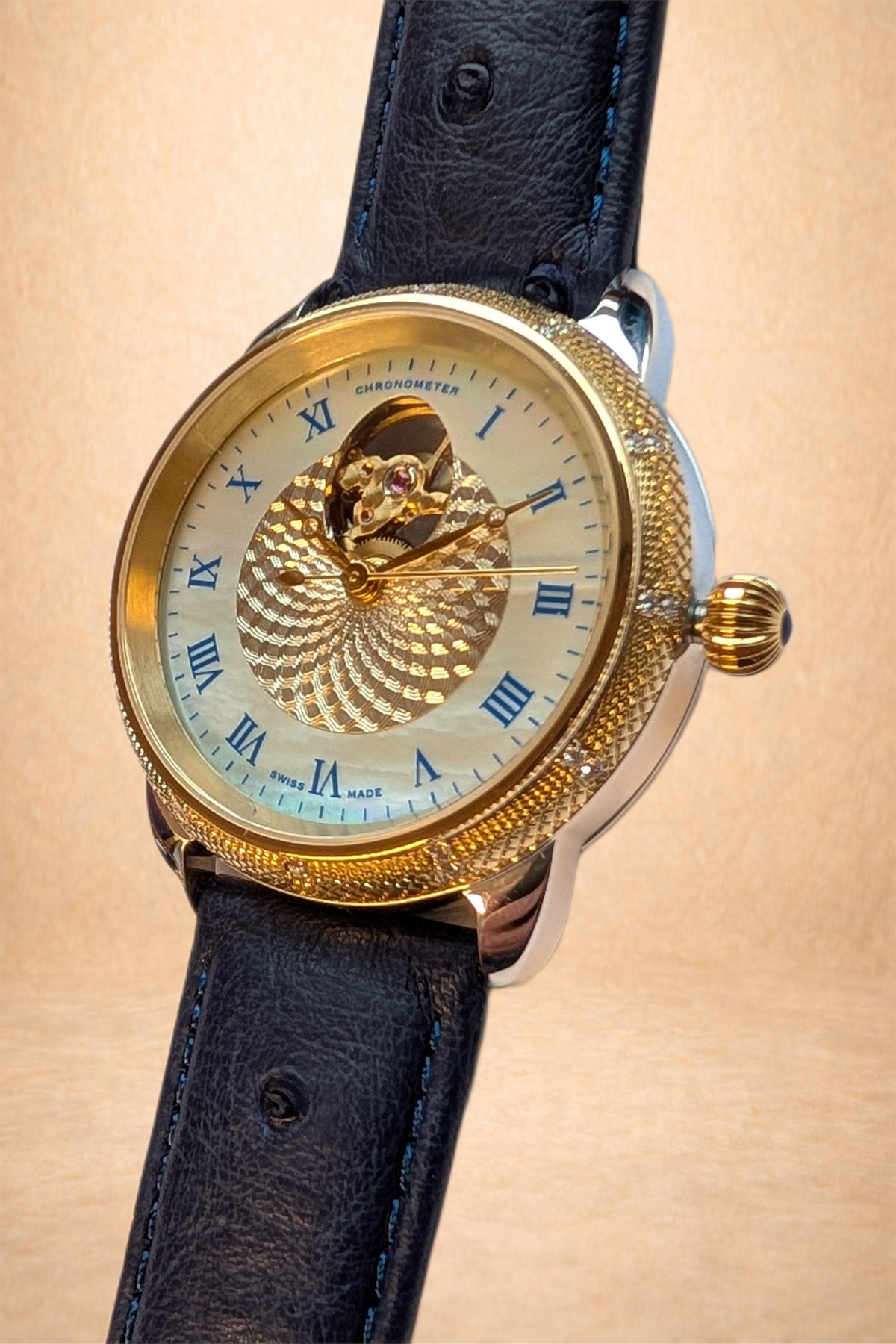 Close-up of a luxury wristwatch with a gold bezel, black leather strap, and an intricate golden dial with blue Roman numeral hour markers and spiral design, showing the watch's inner mechanics.