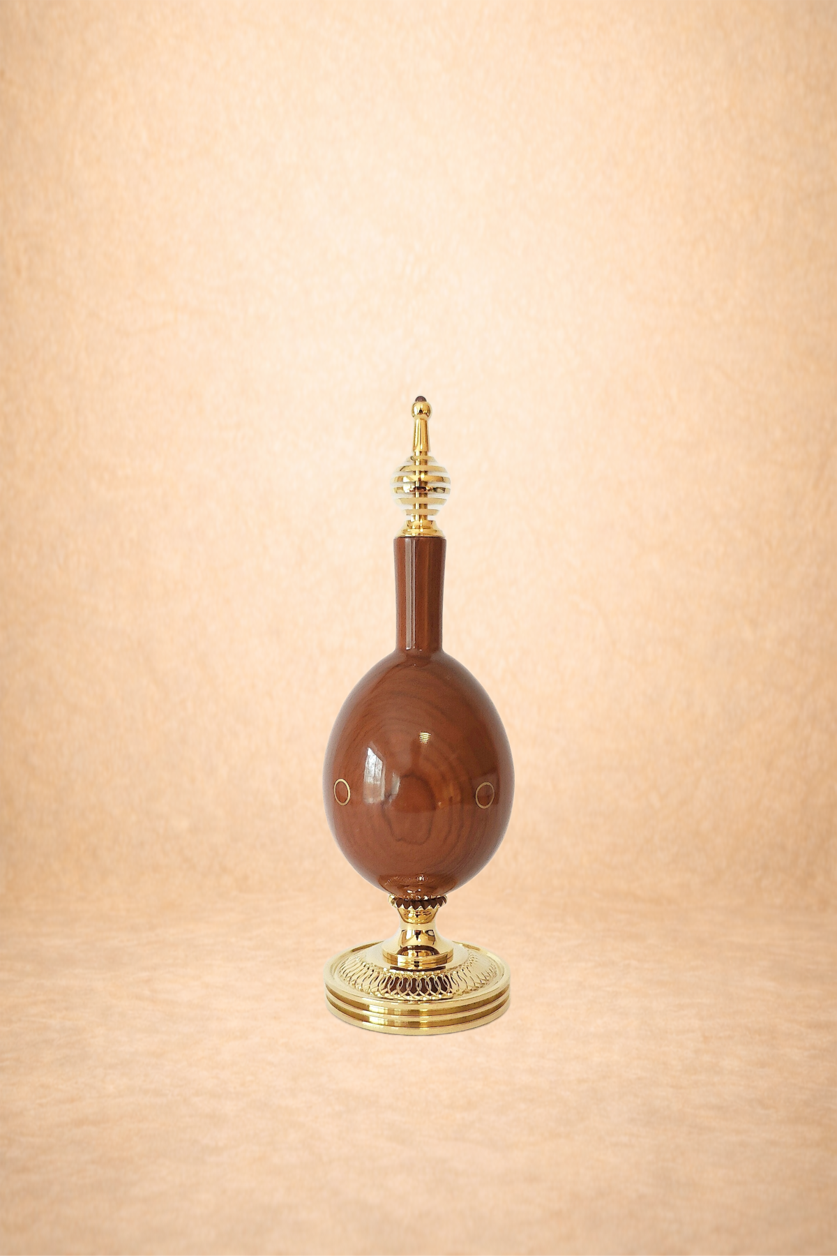 A vintage decorative perfume bottle with a wooden body, gold accents, and a gold and glass top, set against a beige background.