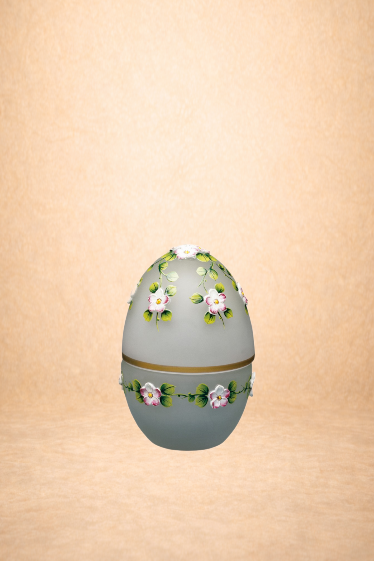 Decorative ceramic egg with pink and white flowers and green leaves, reflected on a shiny surface, against a warm beige background.