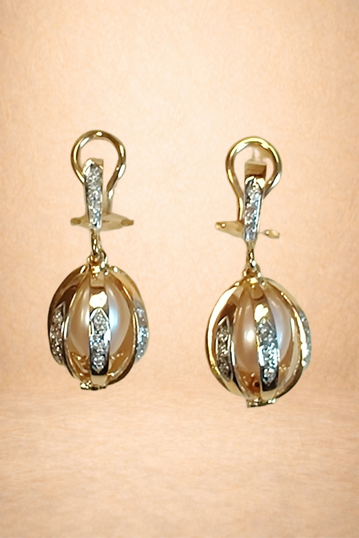 Gold earrings with pearl accents and diamond embellishments hanging against a pink background.