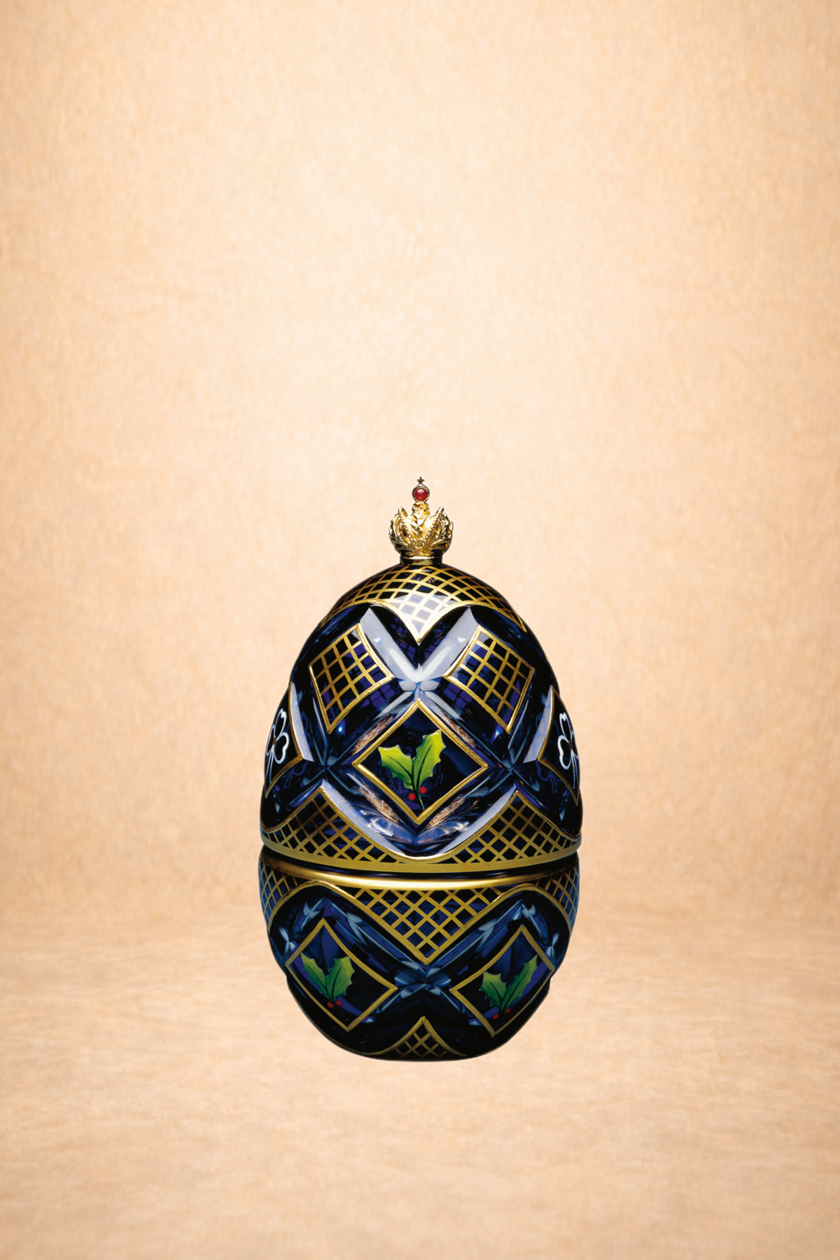 Decorative ornament with holly leaves and berries, reflecting on a surface, set against a beige background.