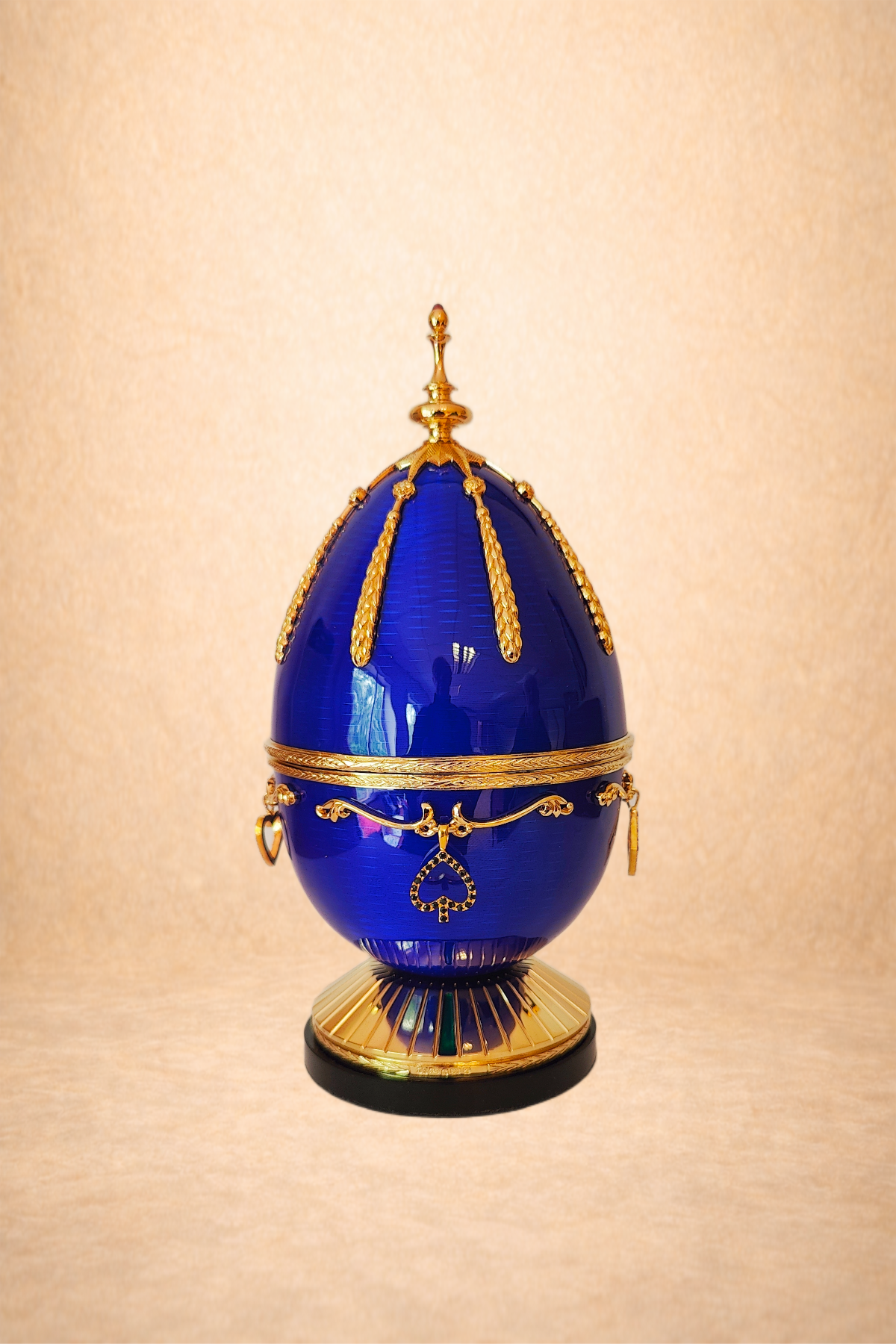 A decorative blue and gold egg-shaped table ornament with intricate gold detailing and accents, set against a beige background.