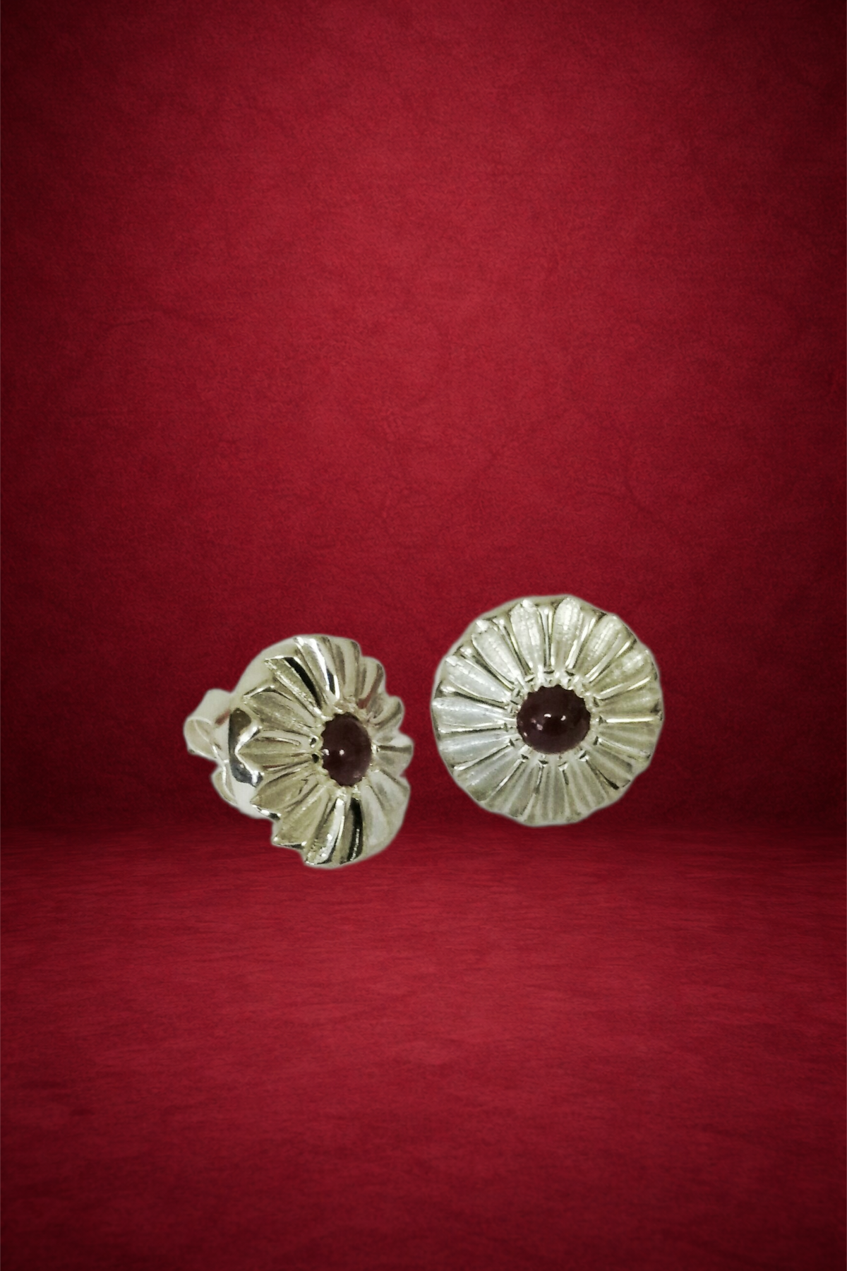 Silver earrings with a flower design and dark central stones, placed on a red background.