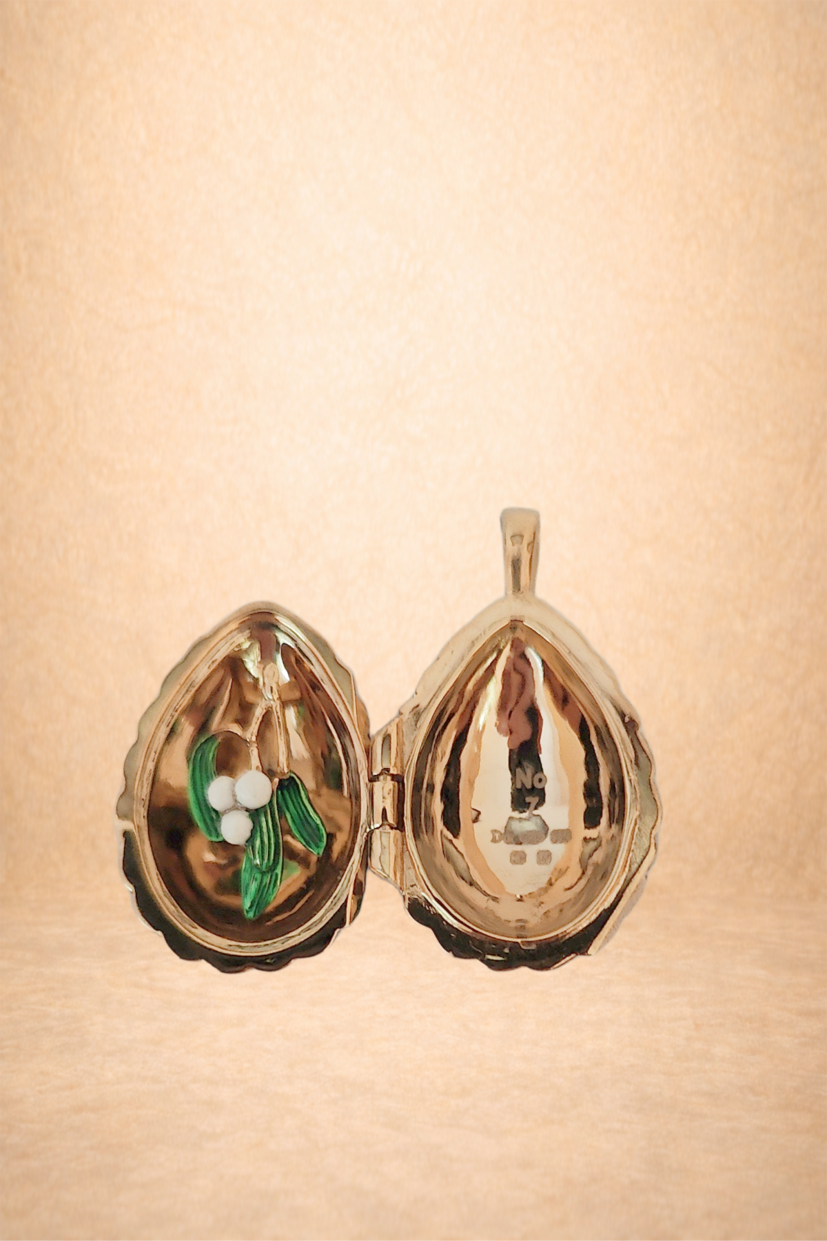 Gold locket in the shape of an olive, with a decorative olive branch and white olives inside, open to reveal the hollow interior.