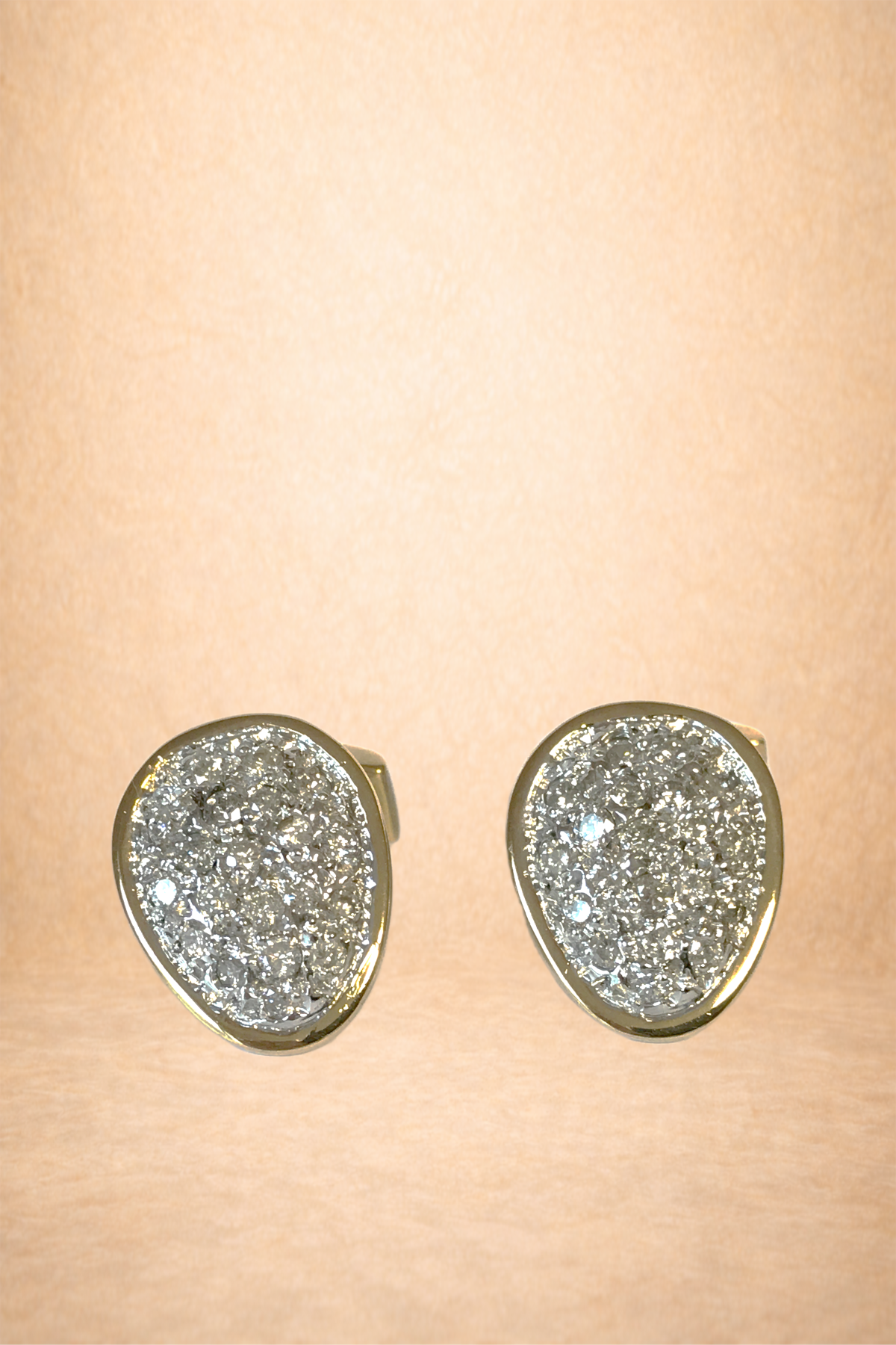 Pair of silver earrings with sparkling rhinestones on a pale pink background.