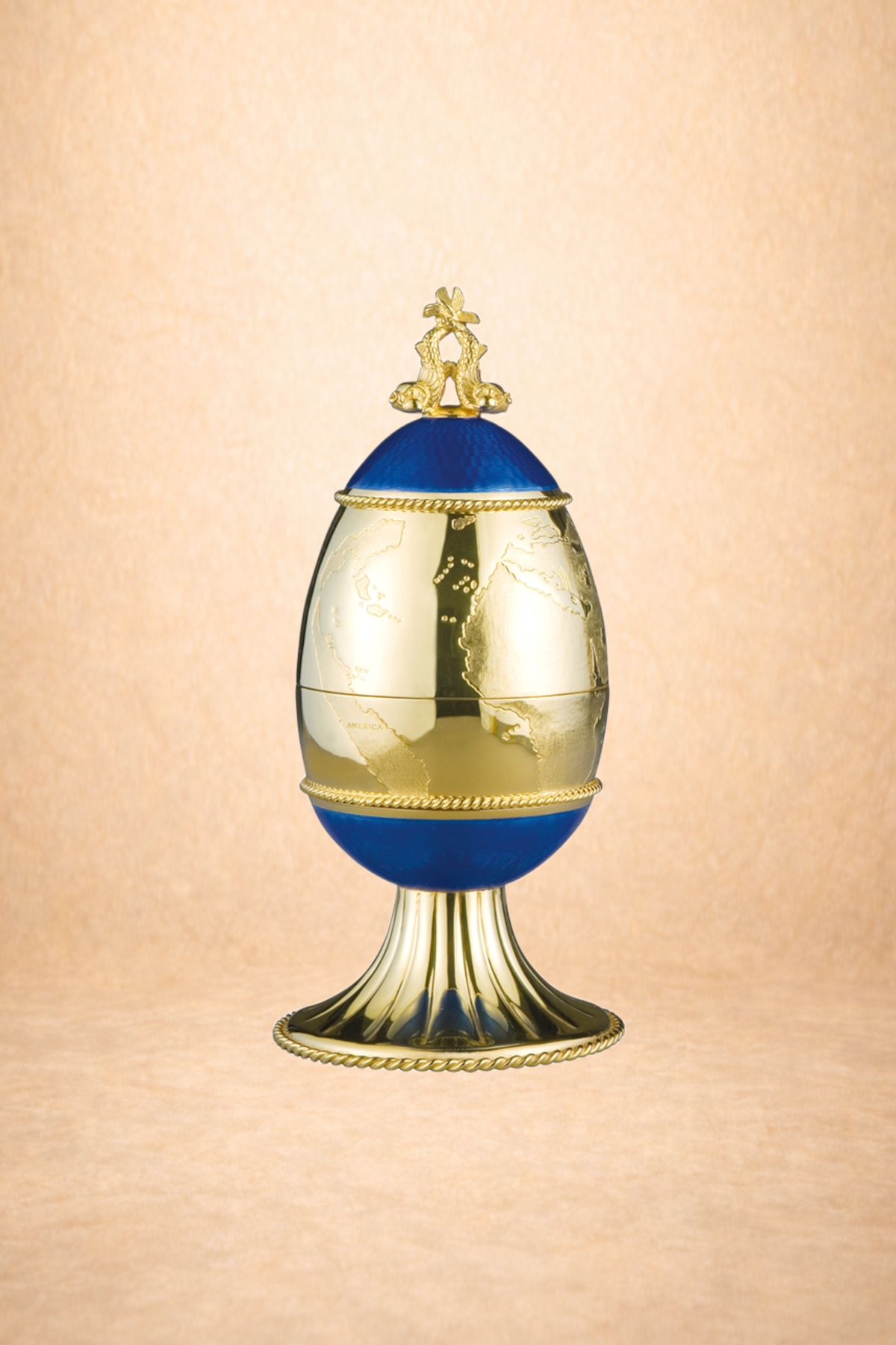 Golden egg-shaped trophy with a world map design, topped with two mice figures, on a decorative stand against a light background.