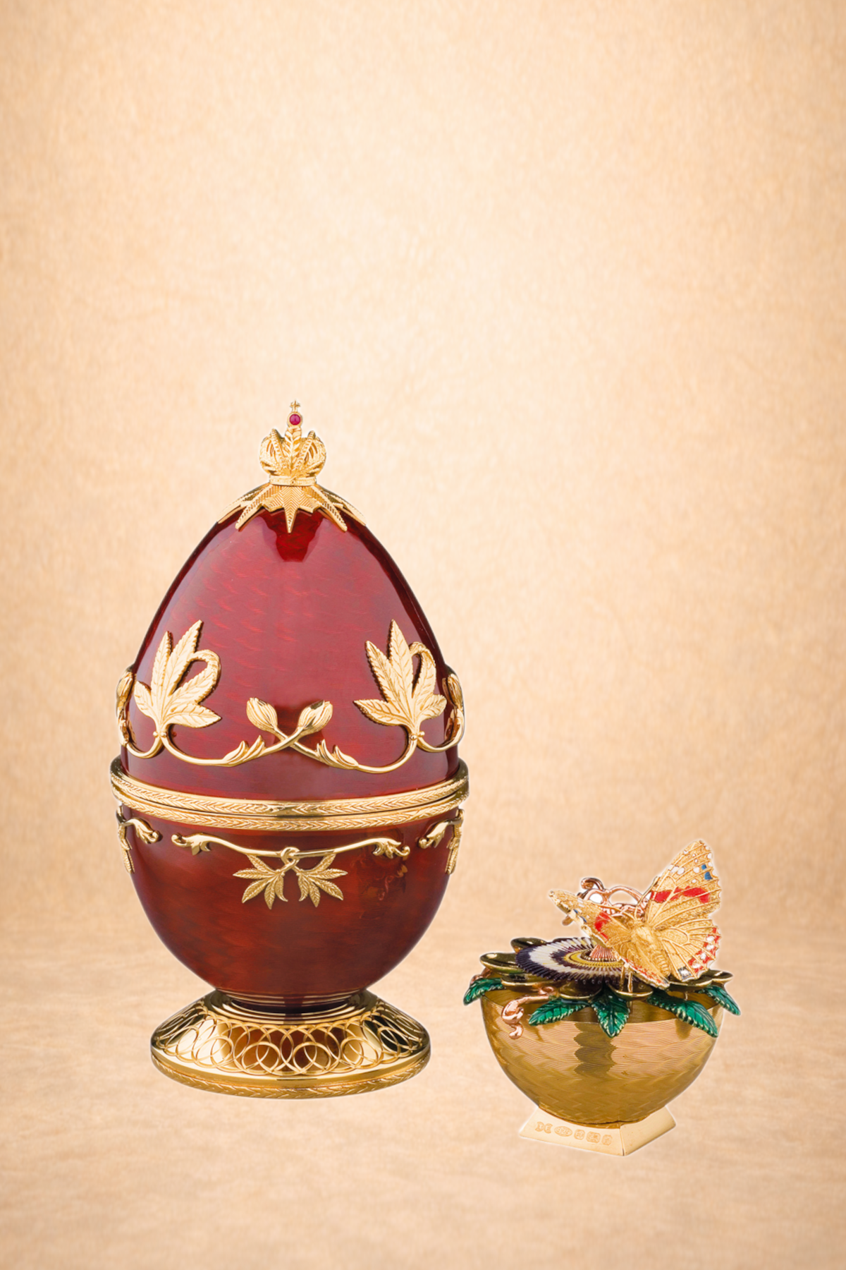Decorative egg with gold floral and crown embellishments on a stand, and a decorative bowl with jewelry and a butterfly ornament on a bed of leaves.