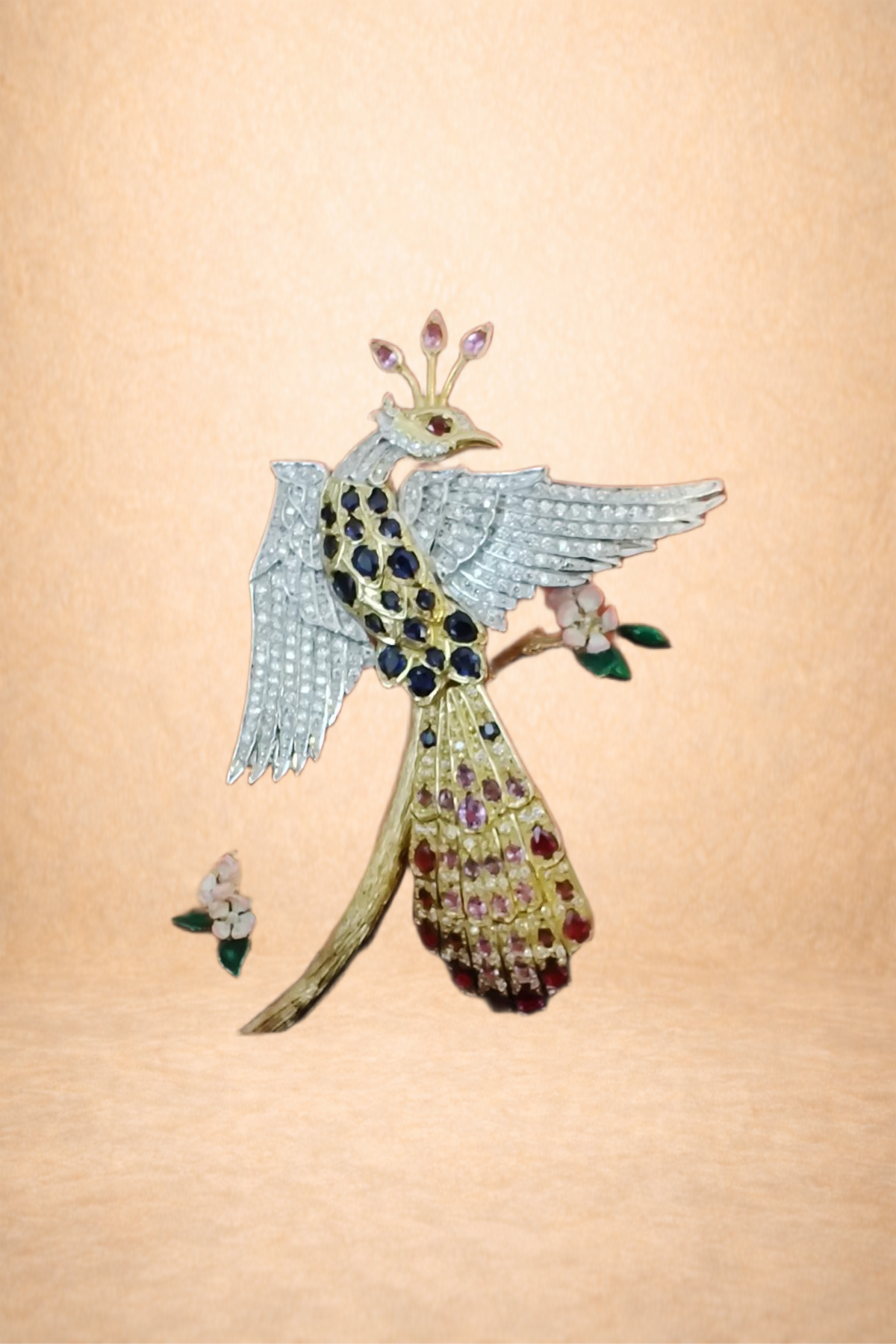 An ornate brooch resembling a peacock perched on a branch with flowers, decorated with multicolored gemstones and intricate metalwork.
