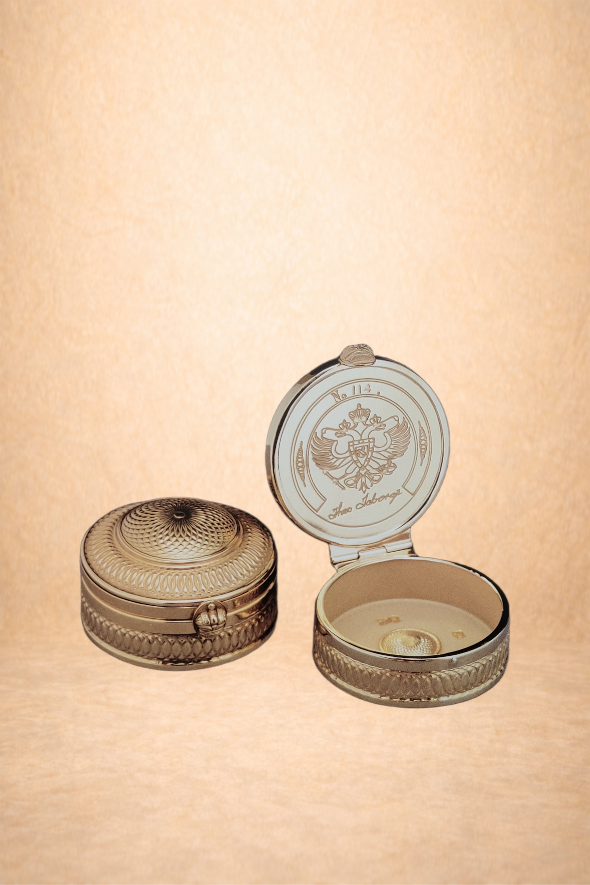 Round silver decorative jewelry box, one closed and one open, with intricate embossed patterns and a coin-like emblem on the inside lid, placed against a textured beige background.