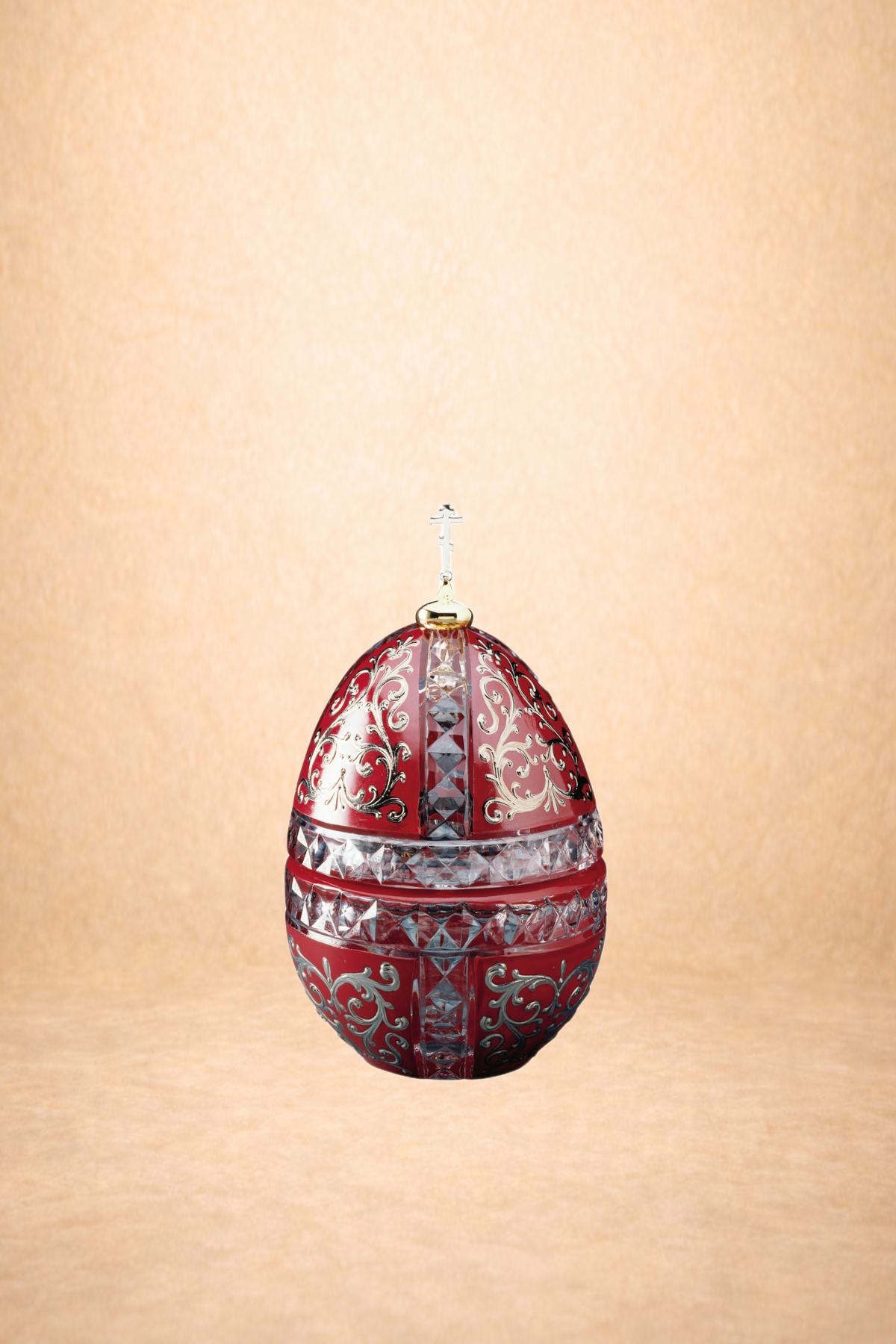 An ornate red and silver decorative egg with intricate silver filigree patterns and clear gemstone accents, reflected on a shiny surface against a beige background.