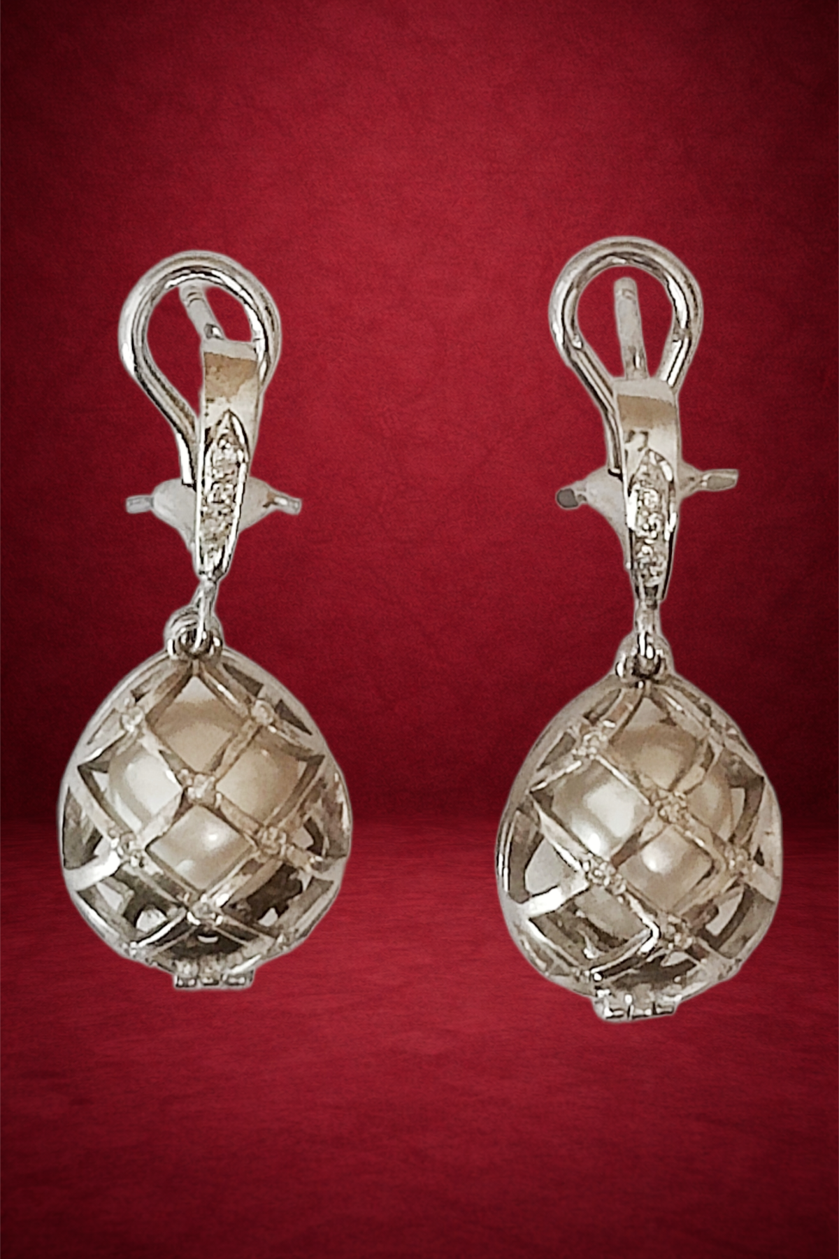 Pair of silver earrings with spherical, lattice-patterned dangles, set against a red background.