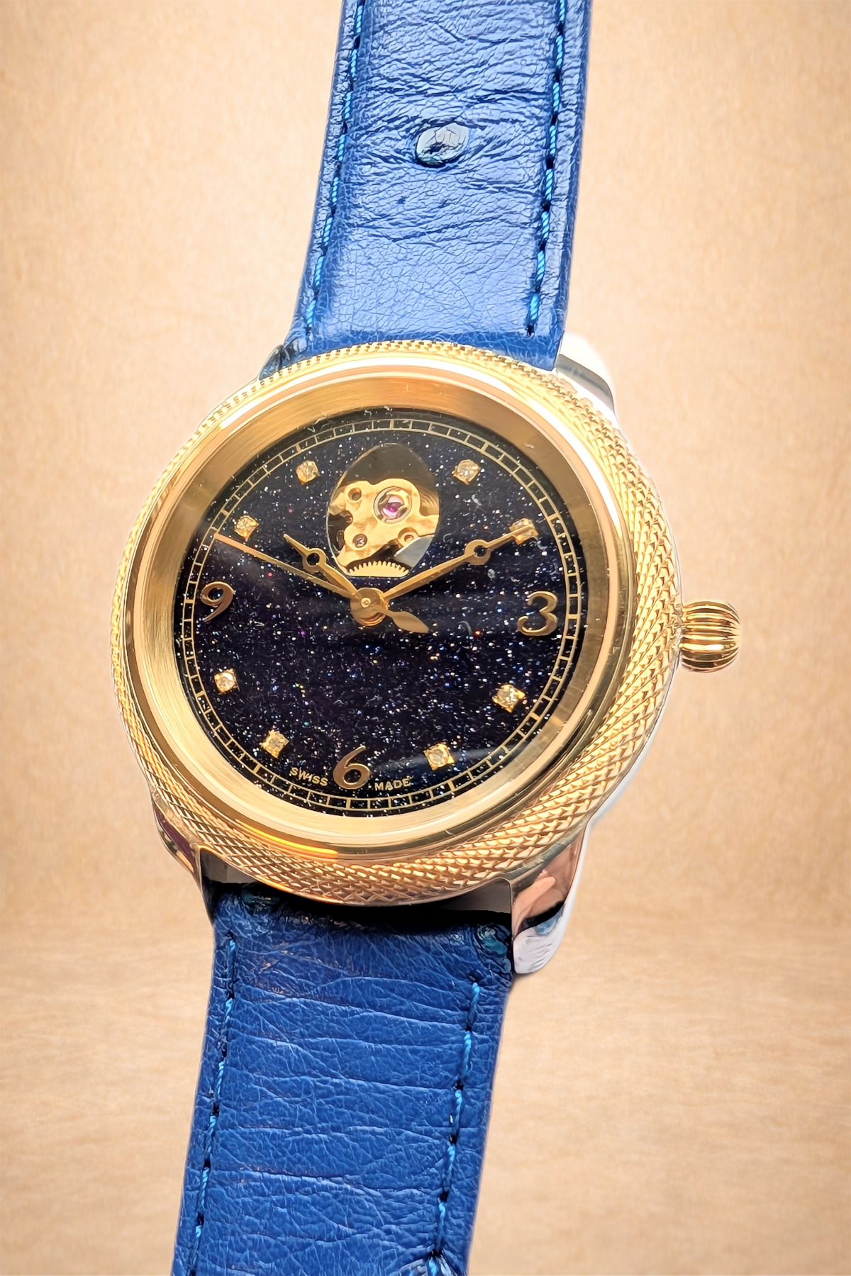 Luxury wristwatch with a gold case, cosmic starry dial, and blue leather strap.