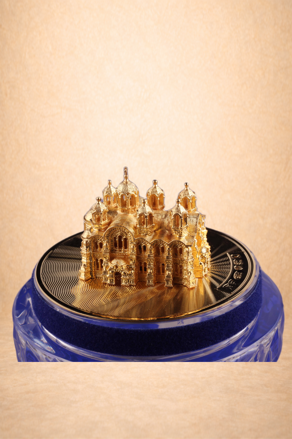 A miniature gold-colored replica of St. Basil's Cathedral on top of a closed sparkling soda can, wrapped in a blue velvet ribbon, with a plain beige background.