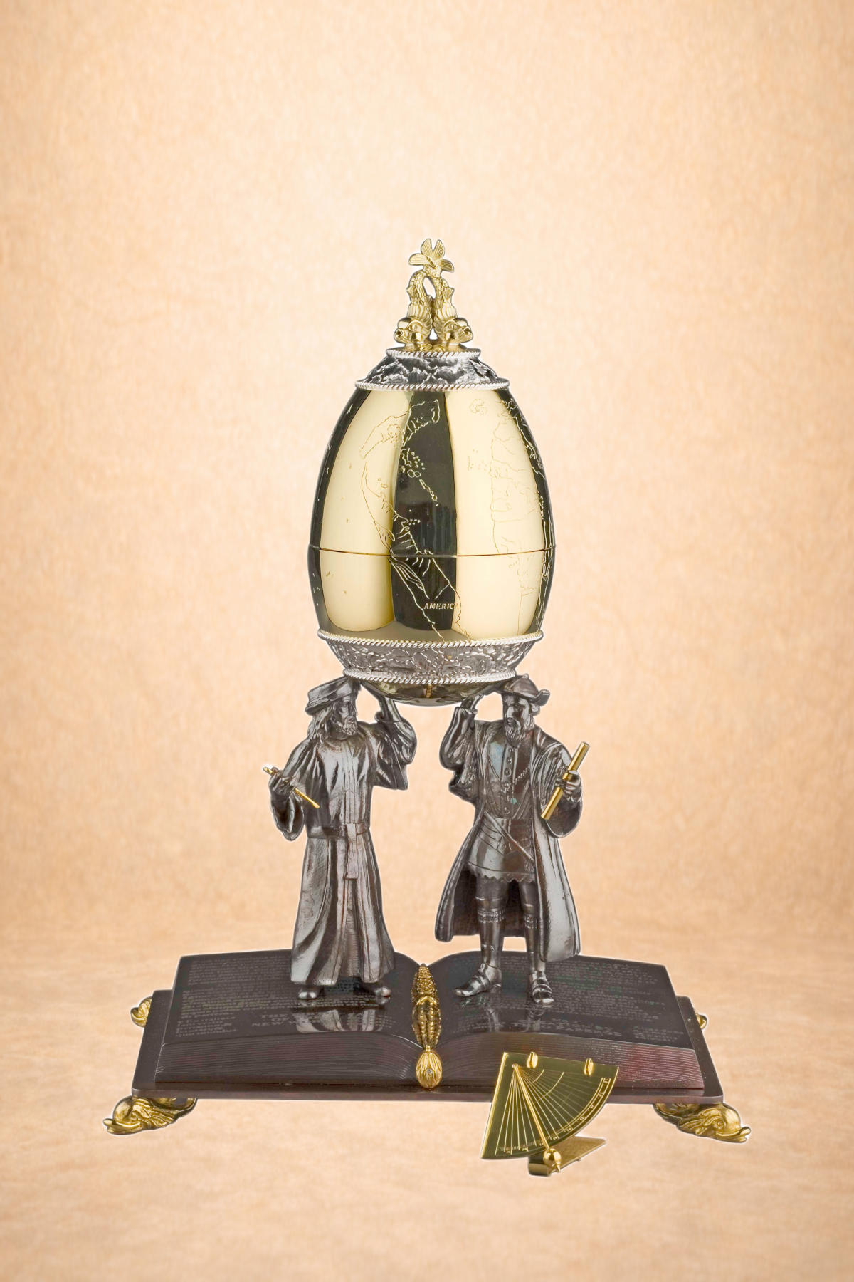 A decorative table clock featuring two human figures in historical attire holding a globe-shaped clock with black and cream segments, topped with an ornamental finial.