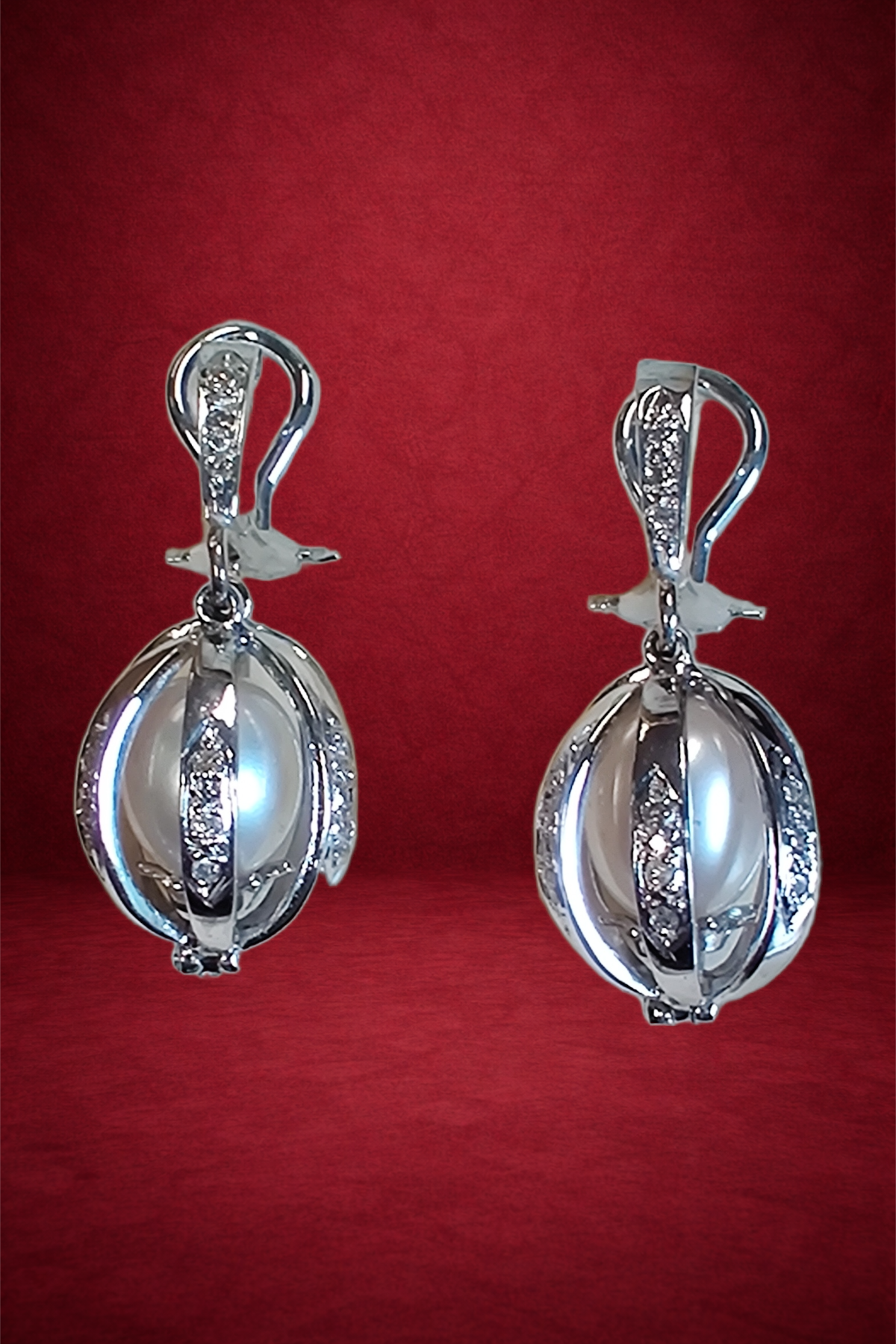 Pair of silver earrings with a spherical design, studded with small diamonds, hanging against a red background.