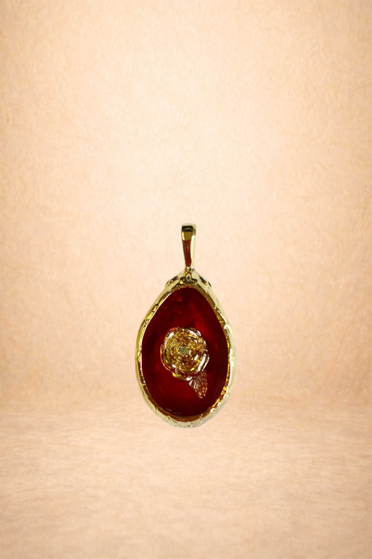 Gold pendant with a red oval background and a raised gold rose design in the center.