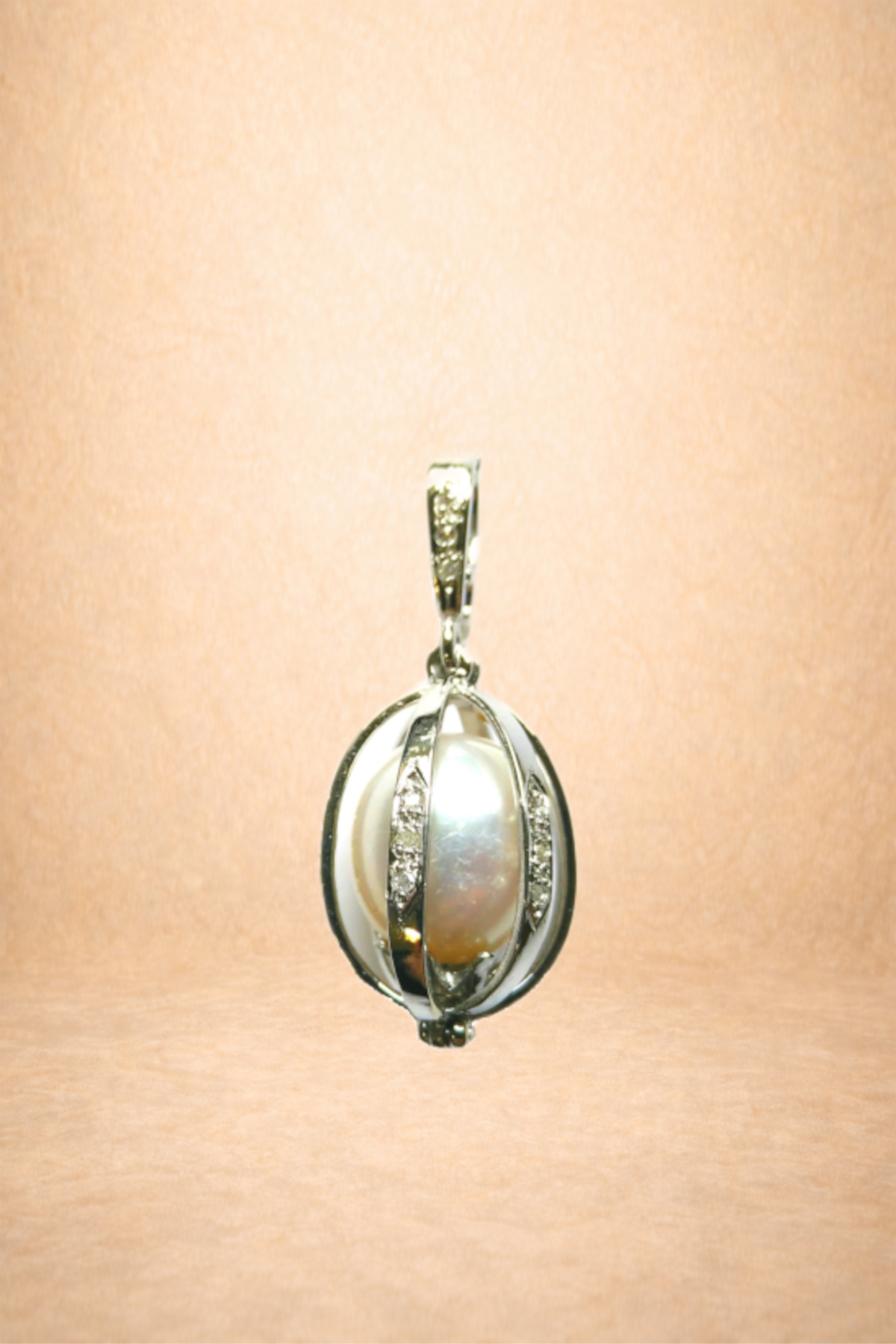 A silver pendant with a centered pearl, encased in a silver frame adorned with small diamonds, hanging against a peach-colored background.