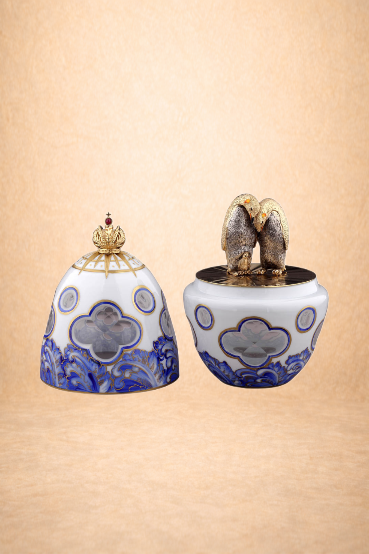 Decorative porcelain container with a gold crown-shaped lid and a figurine of two kissing penguins on top, set against a beige background.