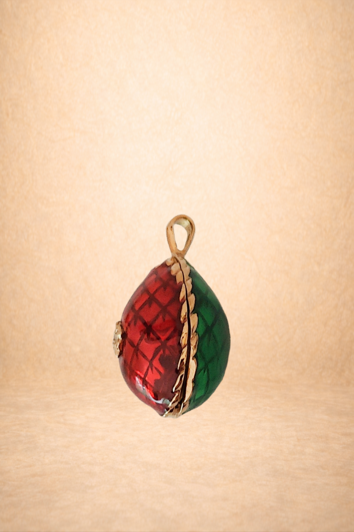 Colorful glass or crystal ornament shaped like a teardrop, decorated with red and green sections and gold accents, hanging against a plain background.