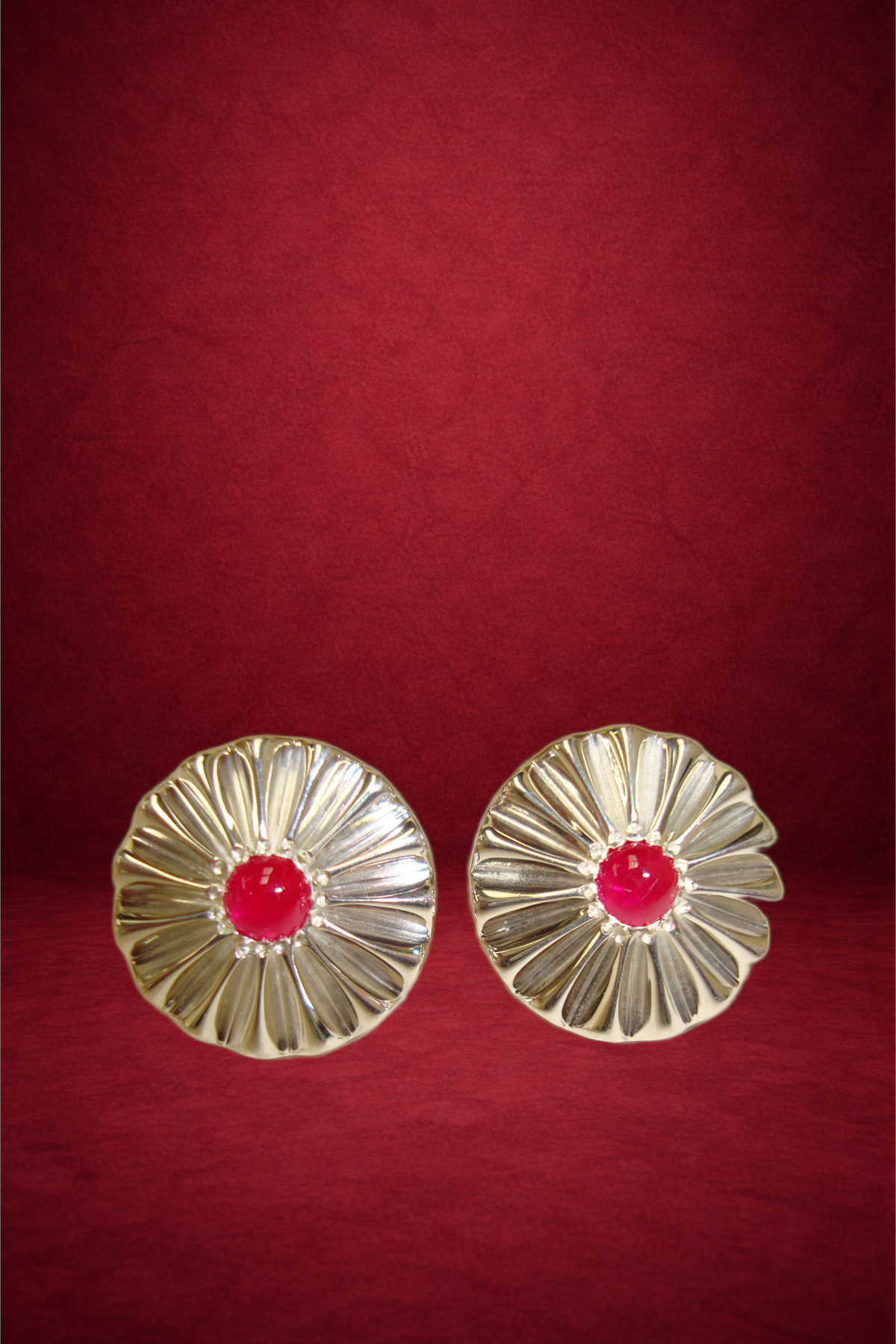 Pair of vintage silver earrings with red centers, placed on a red background.