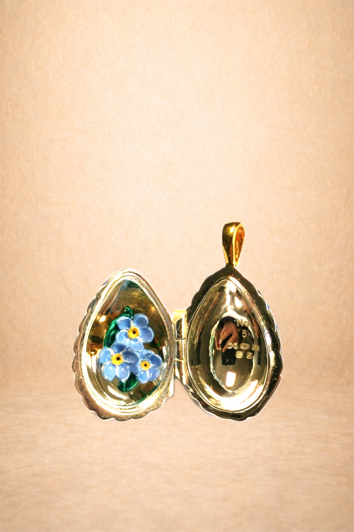 A small, heart-shaped jewelry box with a gold exterior, open to reveal a painted blue flower design on the inside lid and a hollow interior on the right side.