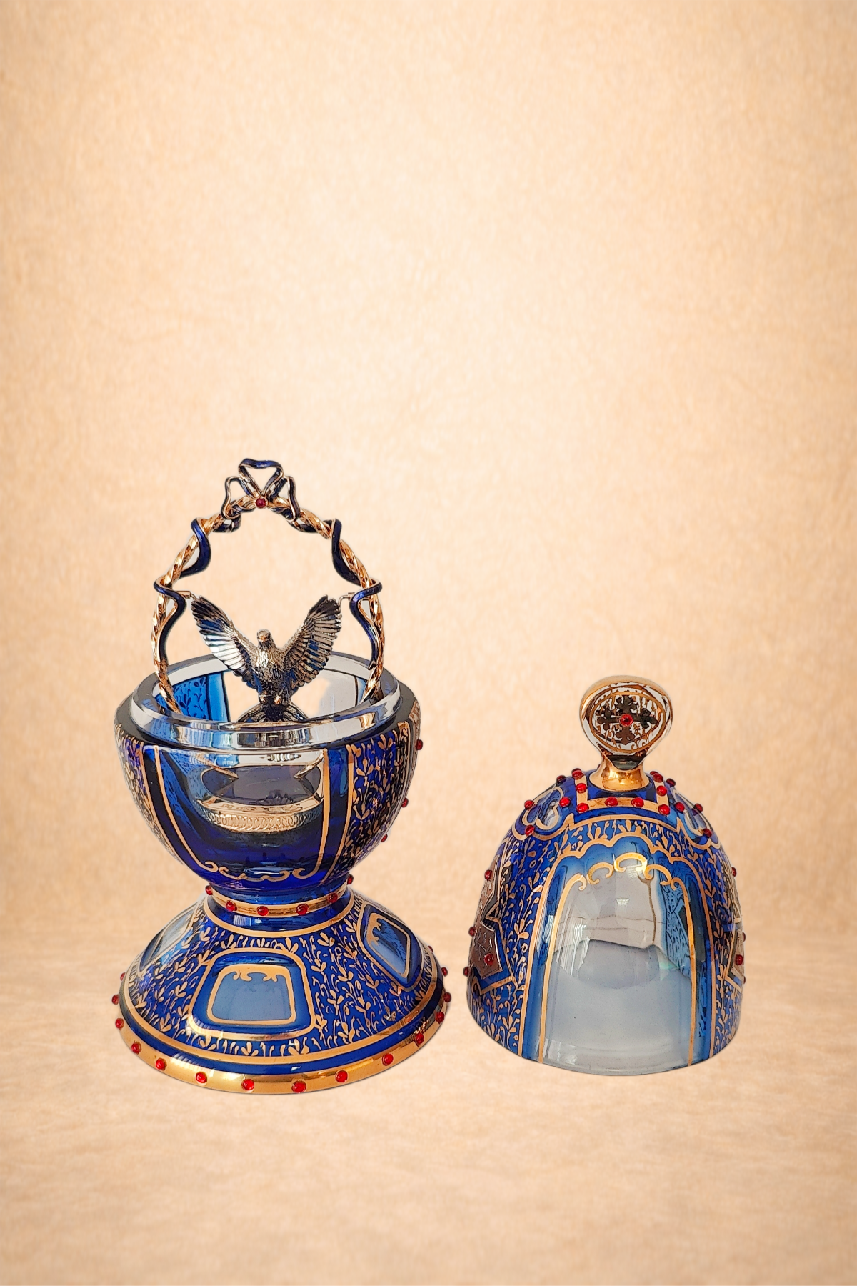 Two ornate perfume bottles with blue and gold designs, red embellishments, and decorative accents; one has a bird figurine on top and the other has a circular decorative top.