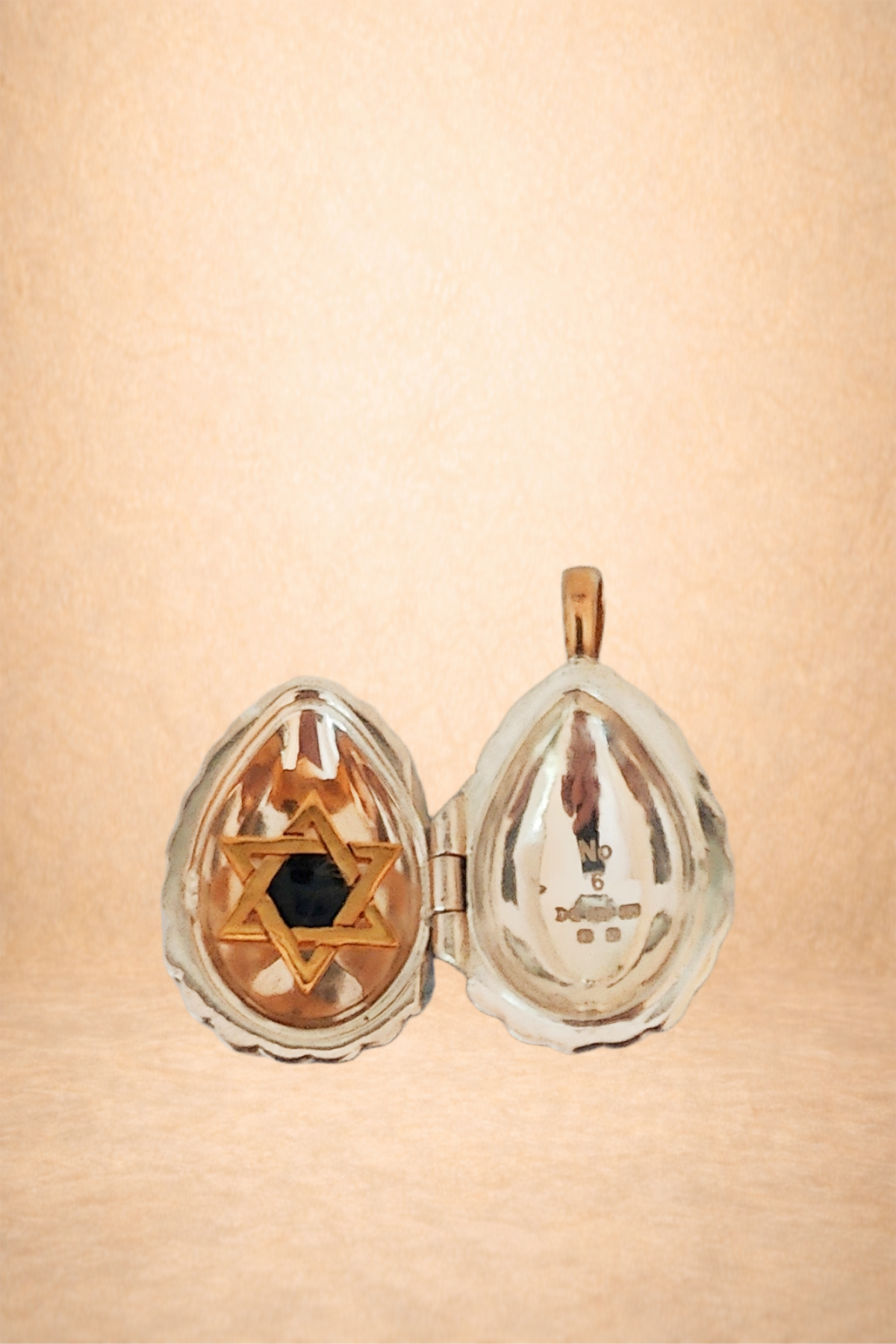 An open glass egg with a gold Star of David inside on the left, and a thermometer on the right, both placed on a flat surface with a neutral background.