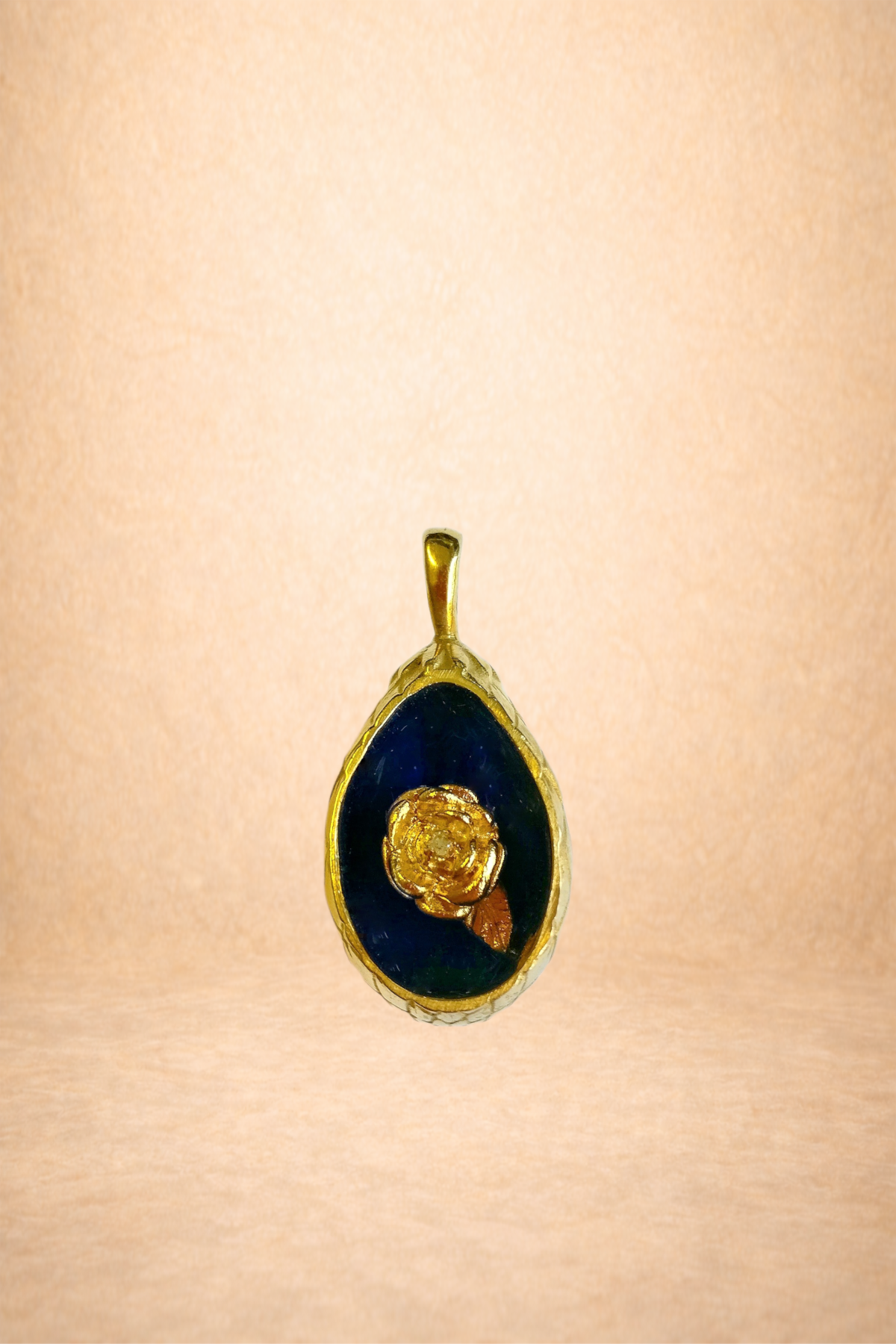 Gold pendant with a dark blue background and a gold flower design in the center, hanging on a light-colored wall.