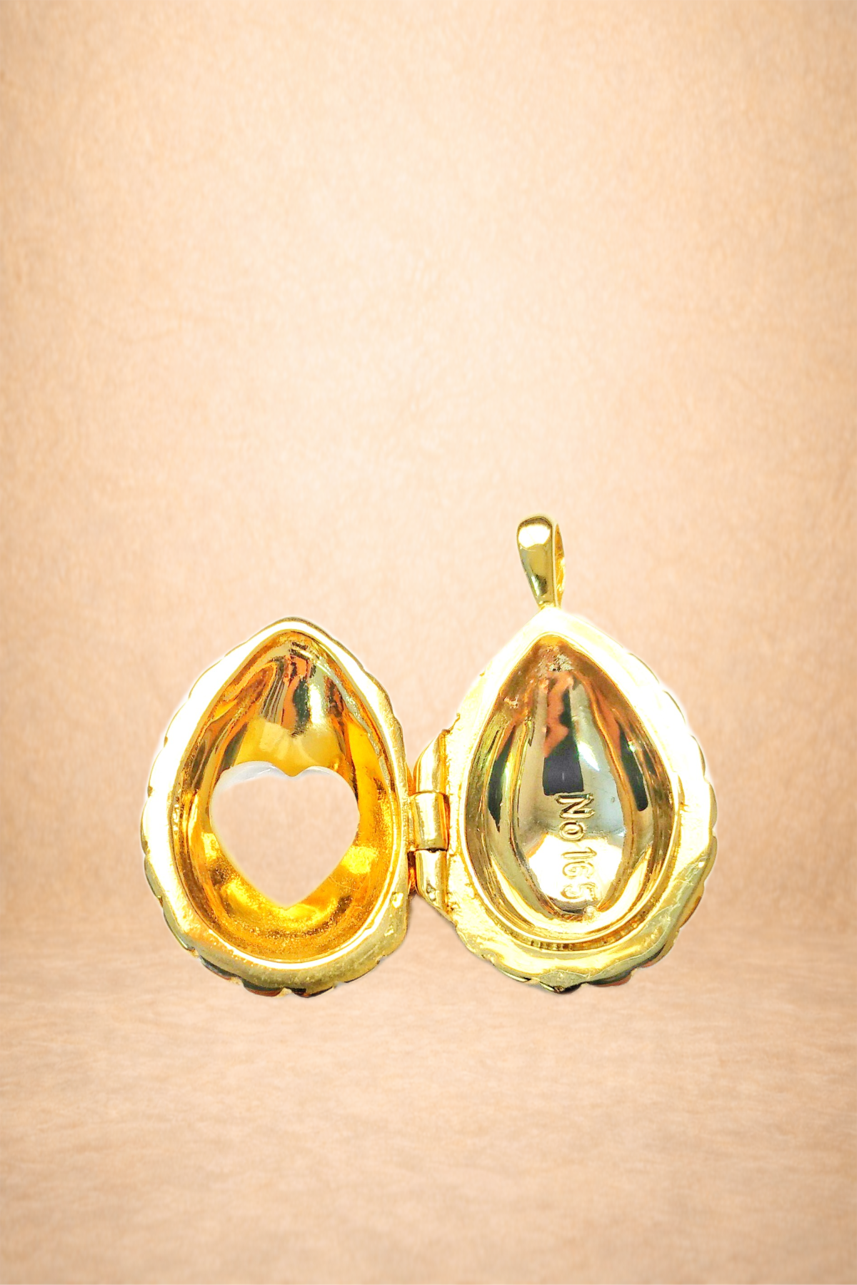 A gold pendant shaped like a walnut, open to reveal a hollow interior with a heart cutout on the left side. The right side is engraved with the number 925 on the inner surface.