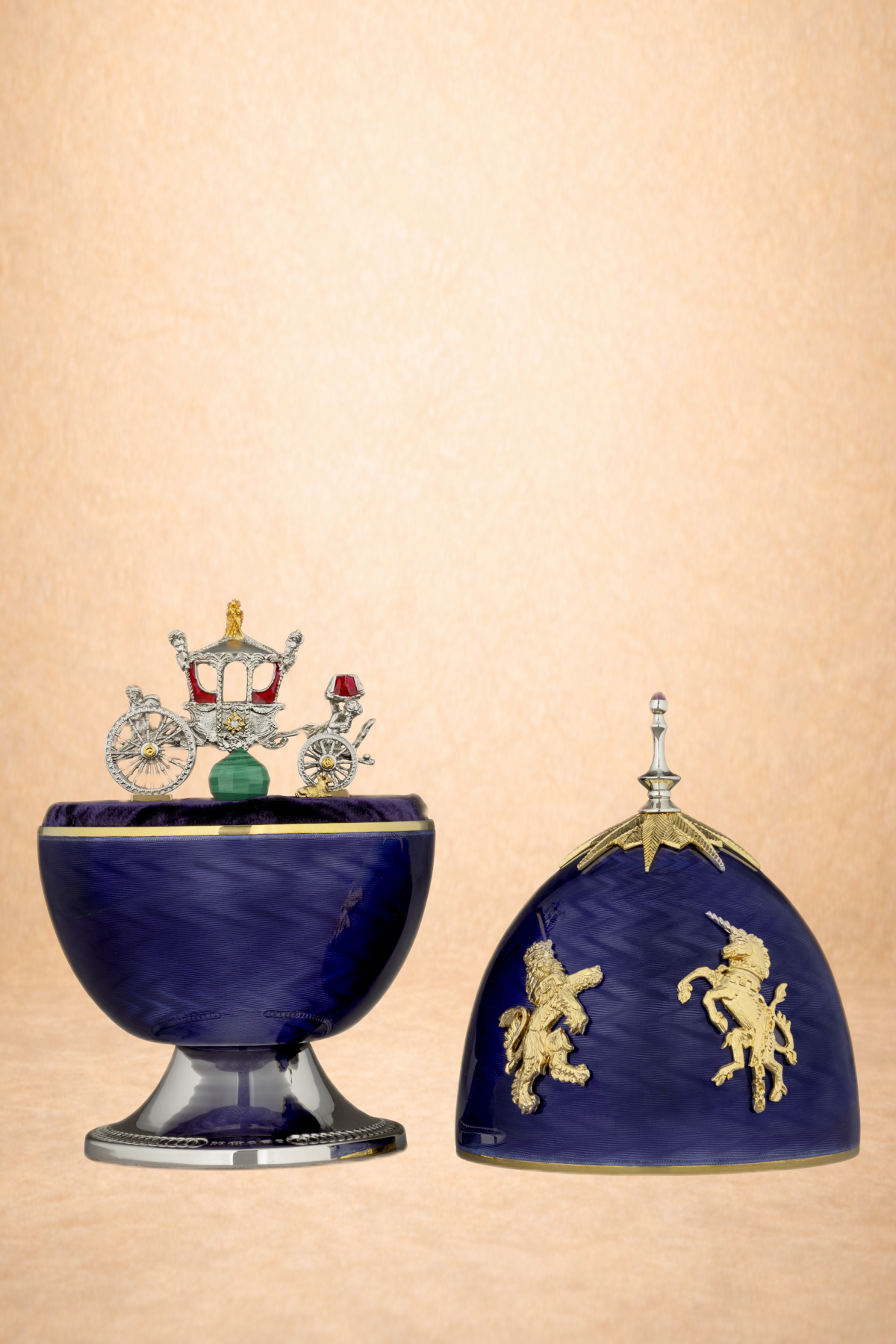 Decorative royal-themed crowns and a miniature royal coach display on a purple velvet-lined stand against a beige background.