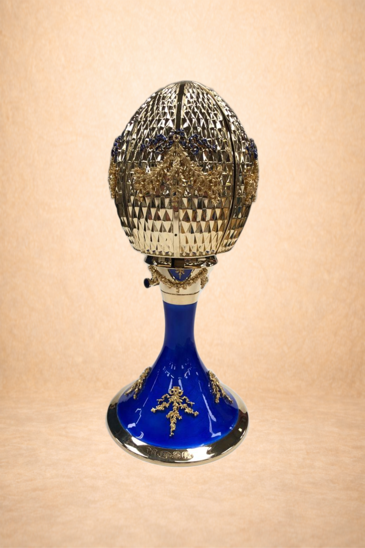 An ornate Fabergé egg with gold and blue accents, featuring intricate detailing and a gemstone embellishment.
