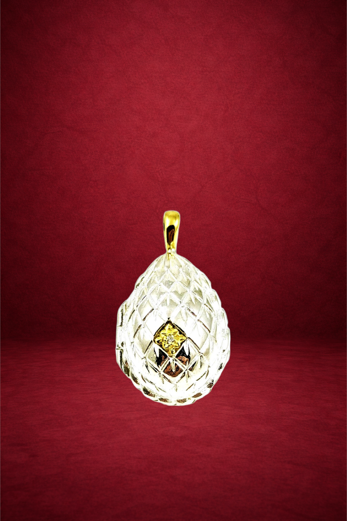 A gold and diamond pendant with a textured, lattice-like design, hanging against a red background.