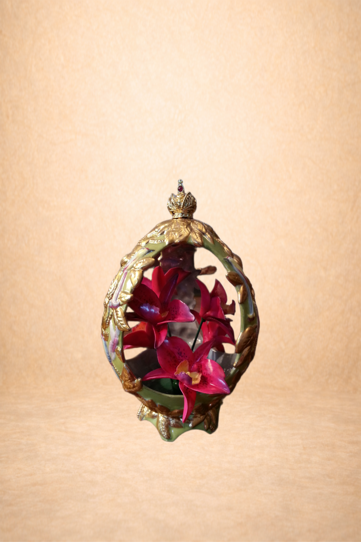 Decorative gold and green ornament with pink orchids inside, topped with a small crown, against a beige background.