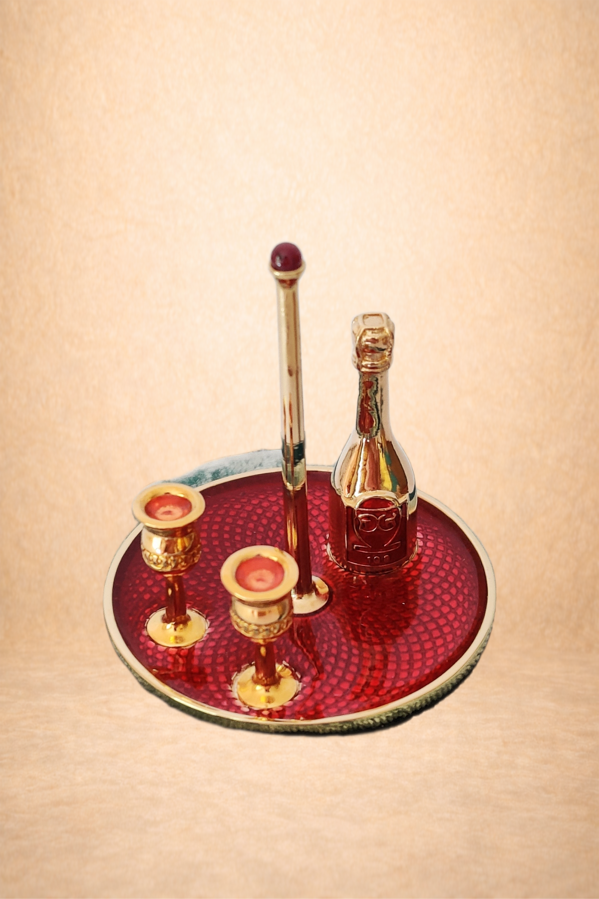 Miniature decorative bar set with gold accents, including a bottle, a tall stick, and three small cups, arranged on a red textured tray.