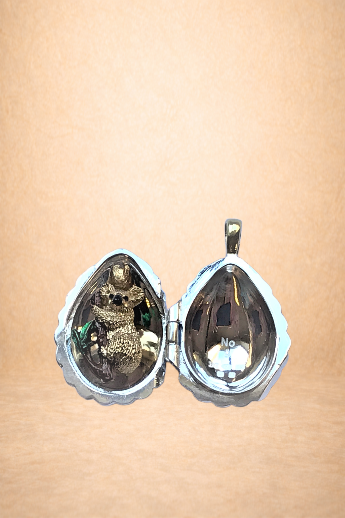 Heart-shaped silver locket with a teddy bear inside the left compartment and the right compartment reflecting light with a faint reflection of the background.