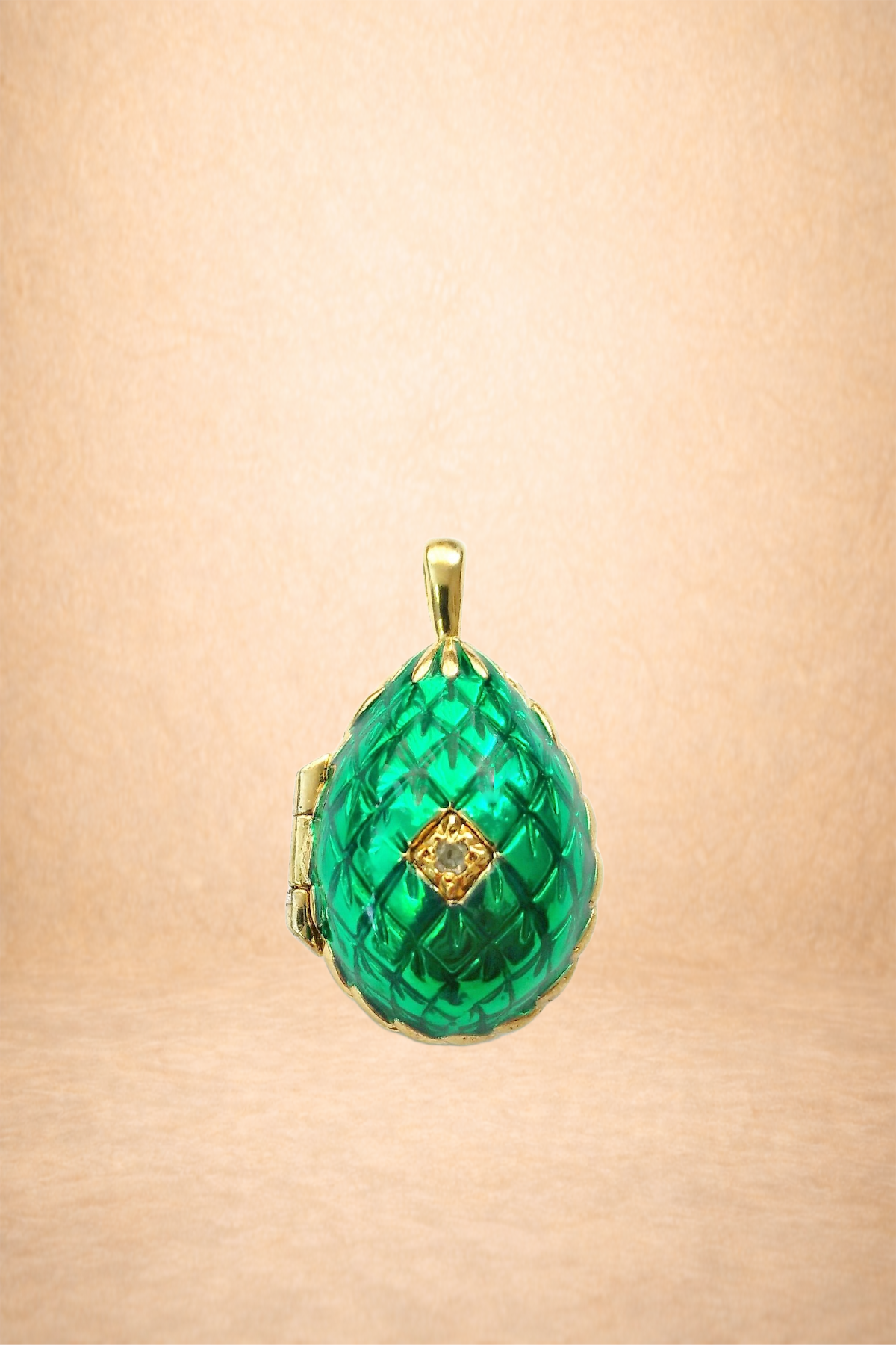 A gold pendant with a large, green, textured gemstone in a teardrop shape, featuring a small diamond in a square gold setting at the center.