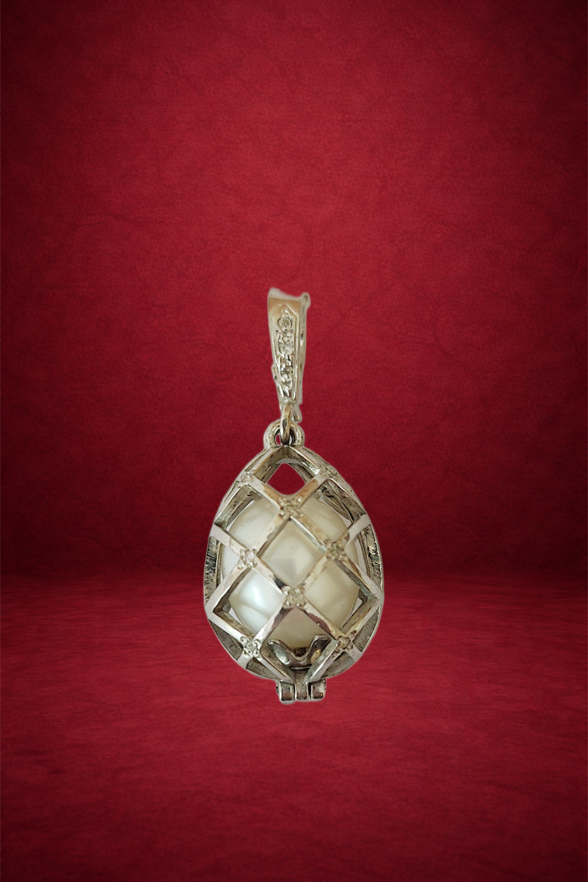 Silver pendant with a white decorative object inside, hanging against a red background.