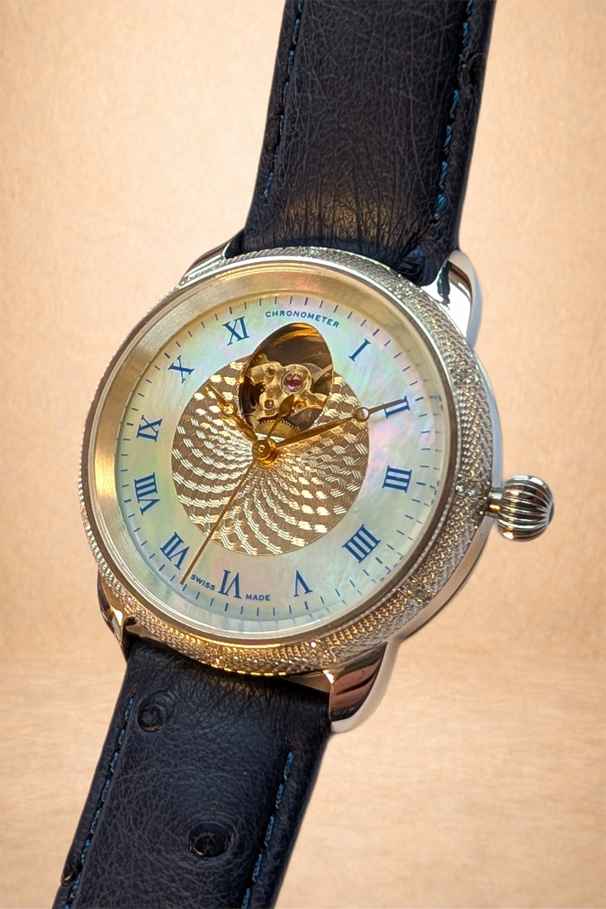 Close-up of a luxury wristwatch with a black leather strap, silver case, and a white face featuring blue Roman numerals, an open-heart design showing the watch's inner mechanics, and gold accents.