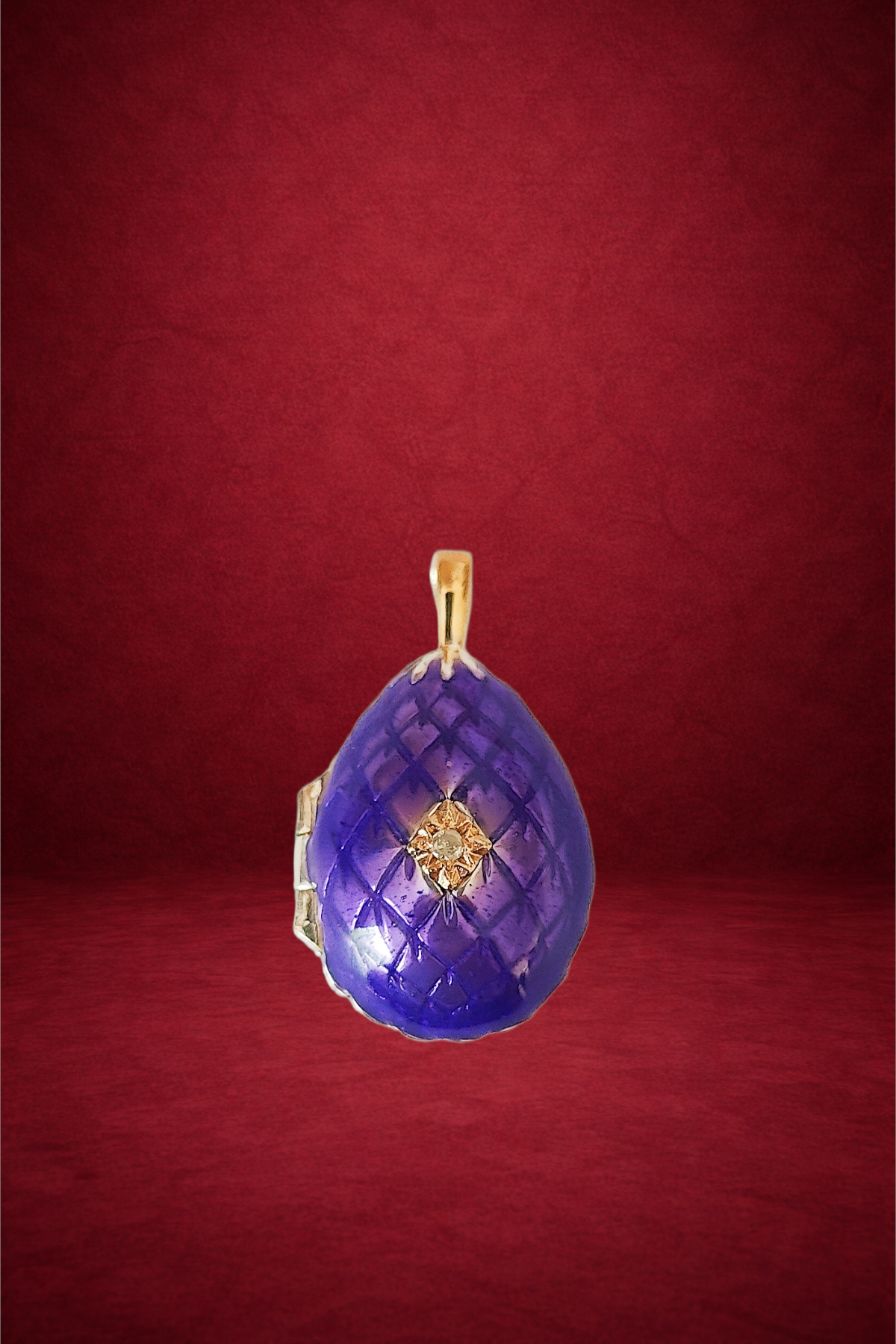 A purple gemstone pendant with a gold bail and a small diamond in the center, set against a red background.
