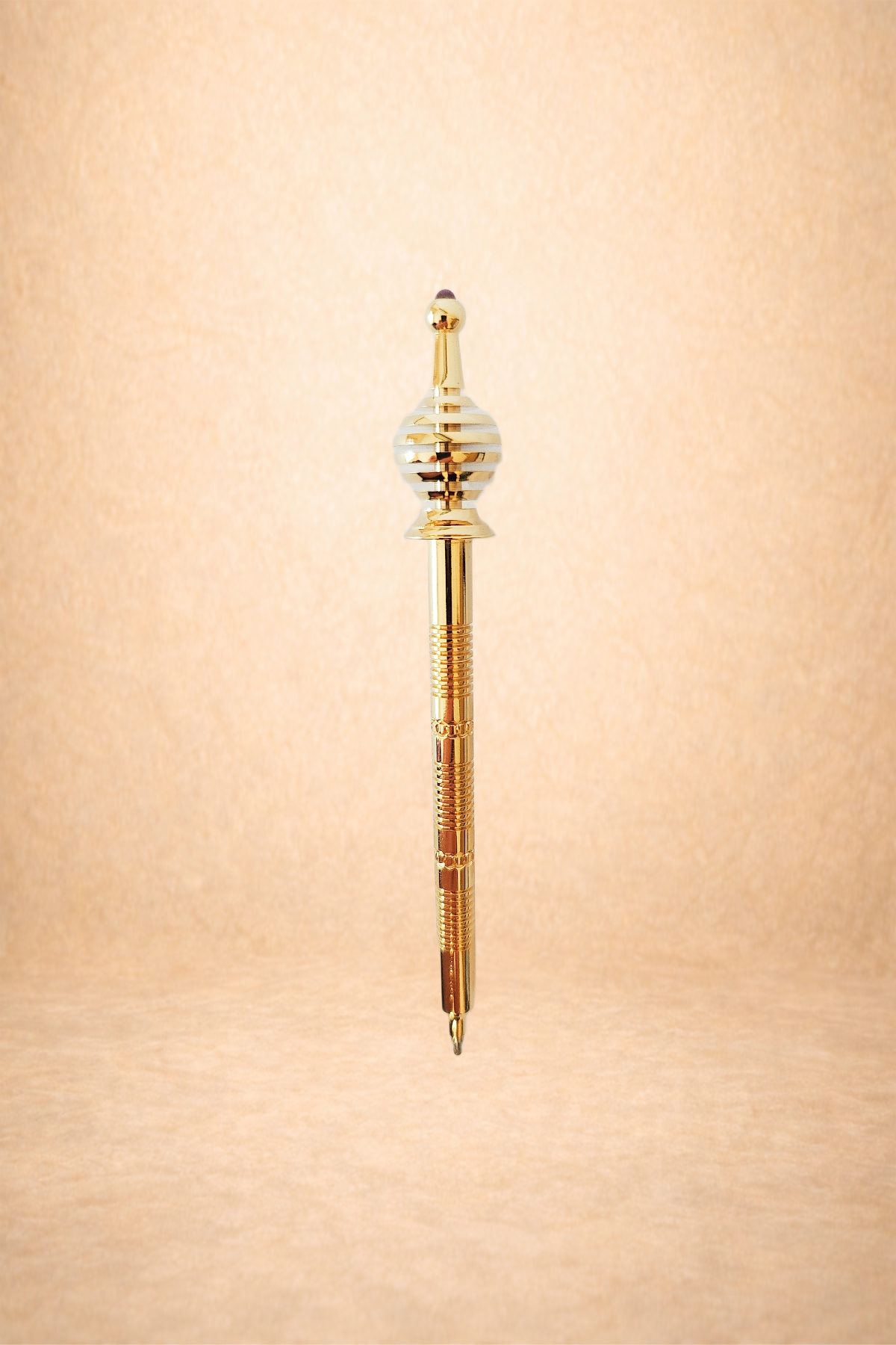 A gold decorative pen with intricate design details, set against a soft beige background.